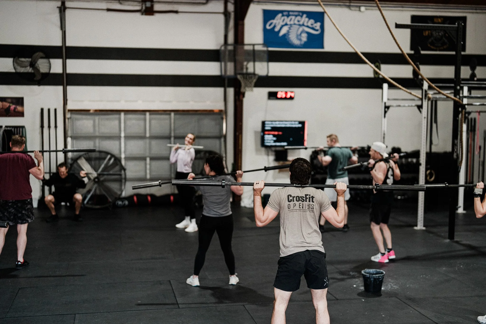 People participating in a CrossFit workout inside a gym, lifting barbells in a group exercise class.