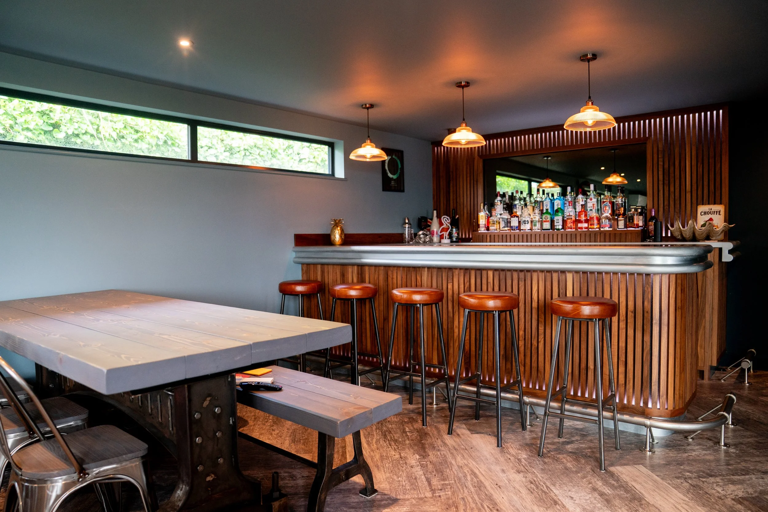 Modern bar area with wood paneling, alcoholic bottles on display, and warm lighting fixtures hanging from the ceiling.