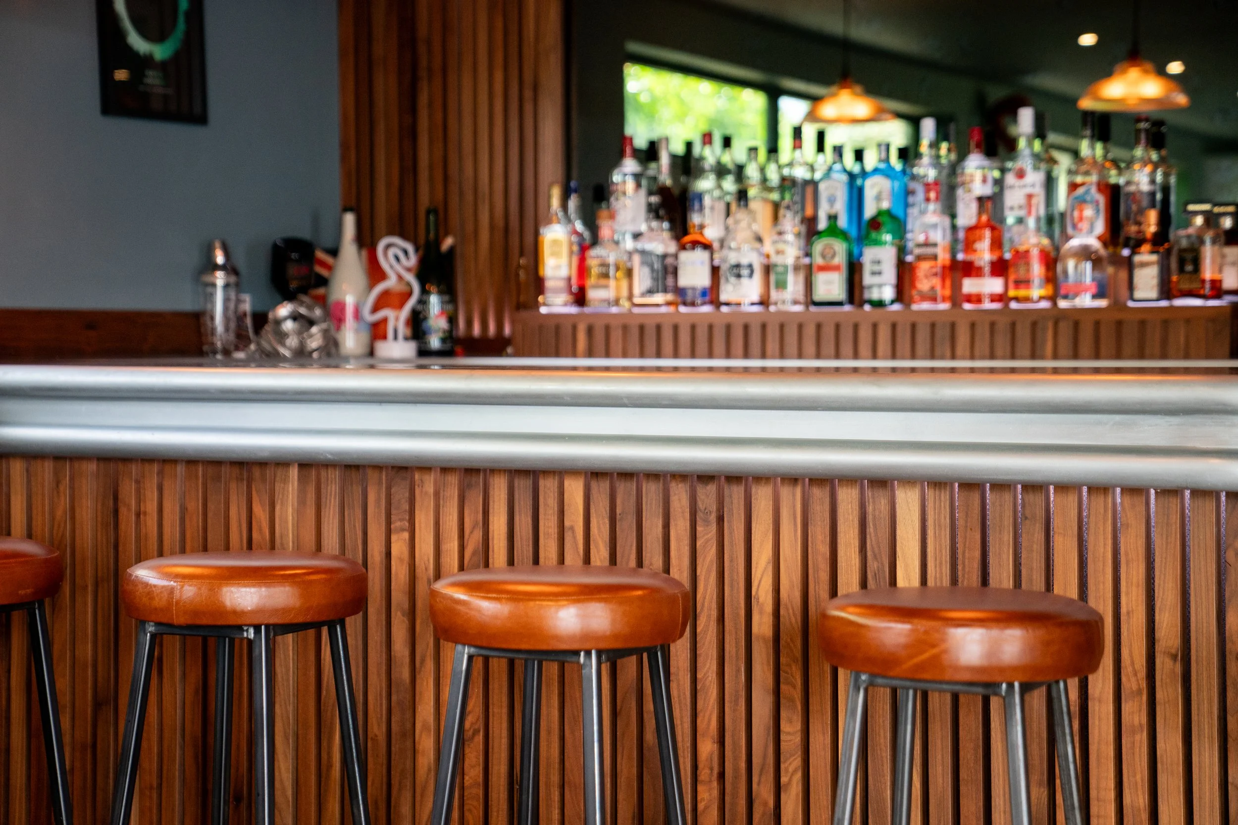 Bar with bottles of liquor on shelves, wooden paneling, and bar stools in the foreground.