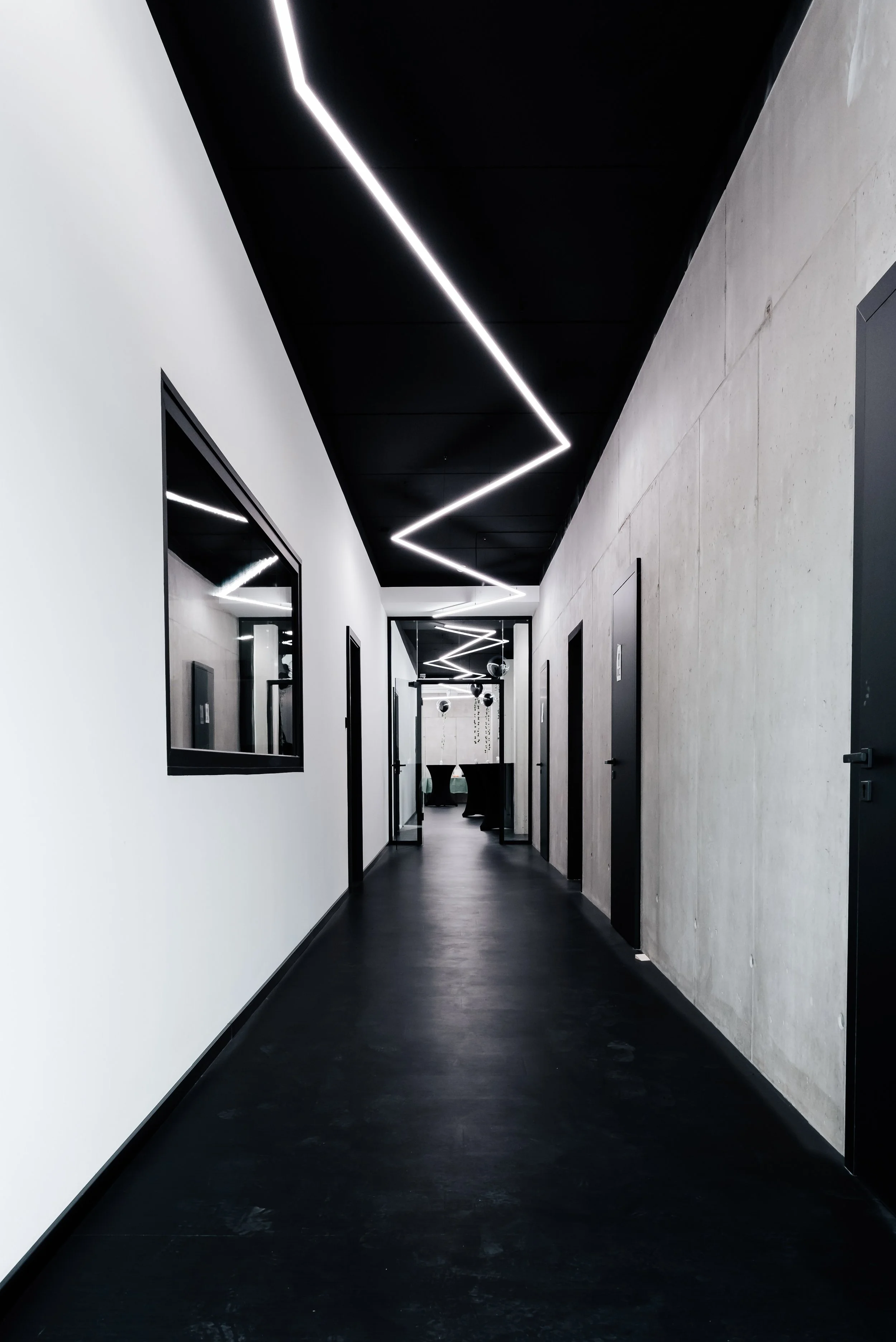 Moderner Flur mit maßgefertigten LED-Lichtlinien, schwarzer Decke und Sichtbetonwand.