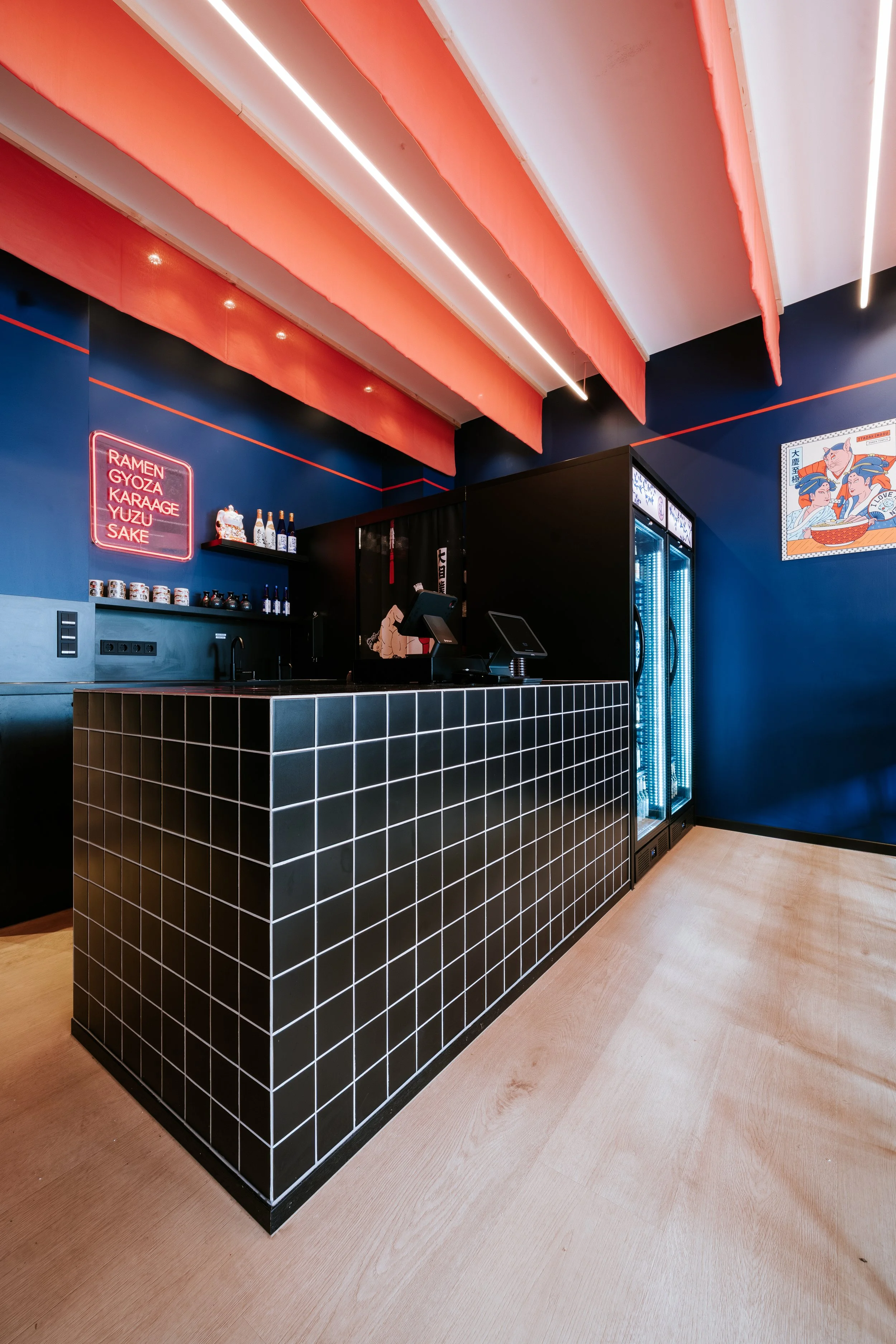 Moderner Bistrobereich mit schwarzer Theke mit weißen Kacheln, blauer Wand, rotem Akzent an der Decke, Neon-Schriftzug mit Speisekarte, Kühlschrank mit Glastür, japanische Wandkunst