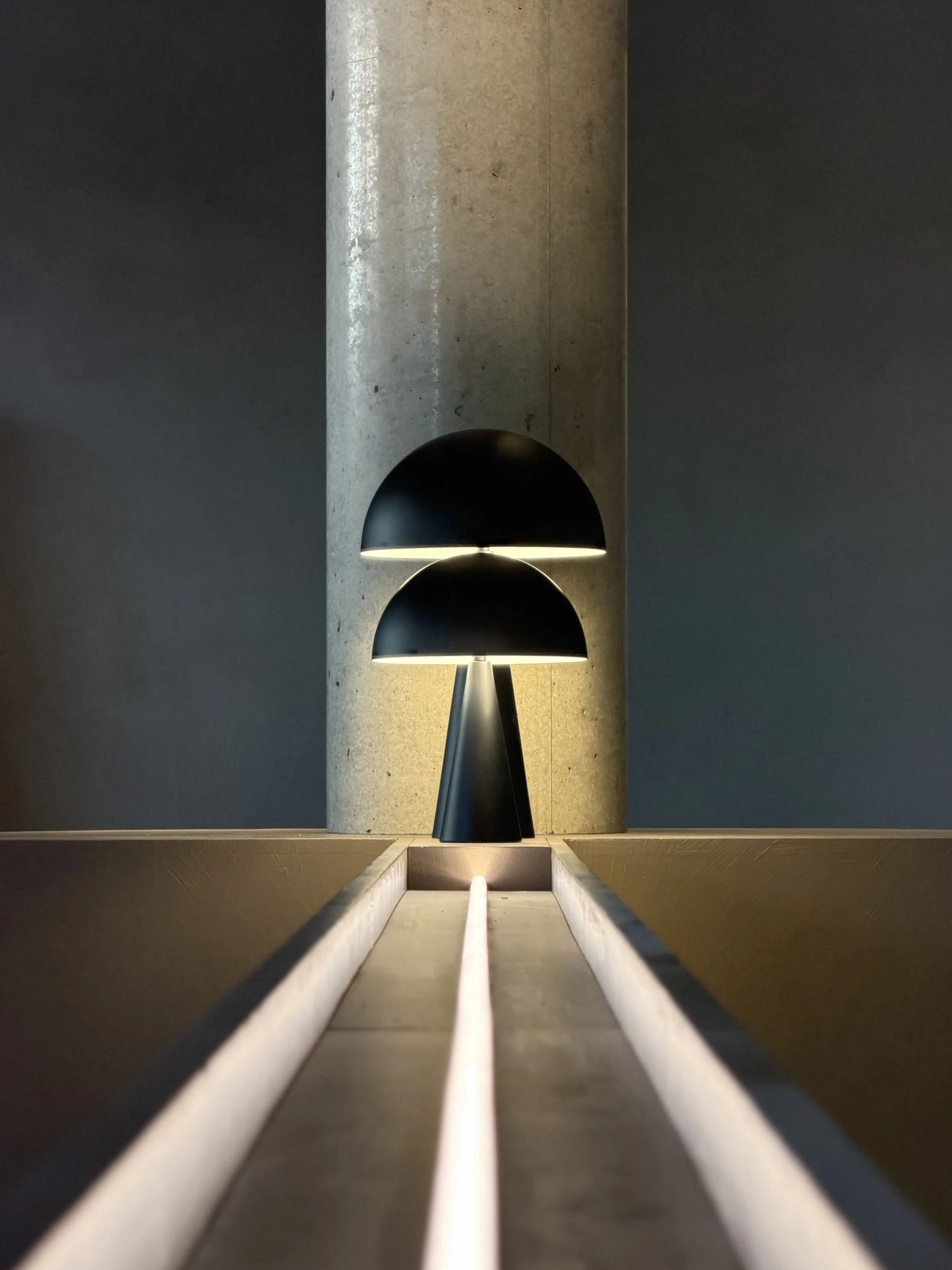 Moderne Leuchte mit zwei schwarzen Halbkugeln an einem Betonbalken, Licht nach unten gerichtet, im Raum mit dunklen Wänden im  T Kitchen in Wetzlar von Stelios Licht-Design.