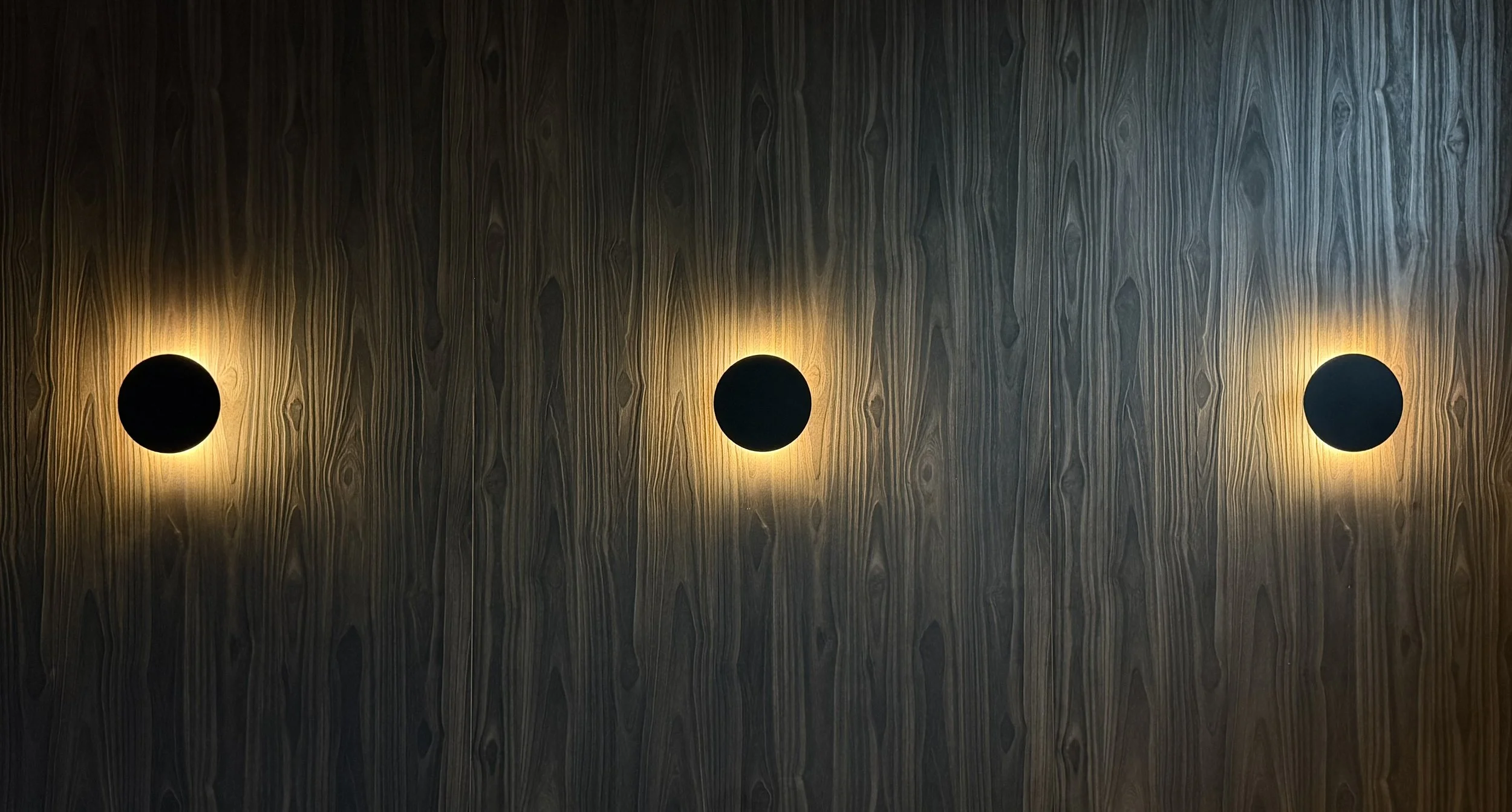 Drei runde Wandleuchten an einer Holzoberfläche, die eine warme Beleuchtung ausstrahlen im T Kitchen in Wetzlar von Stelios Licht-Design.