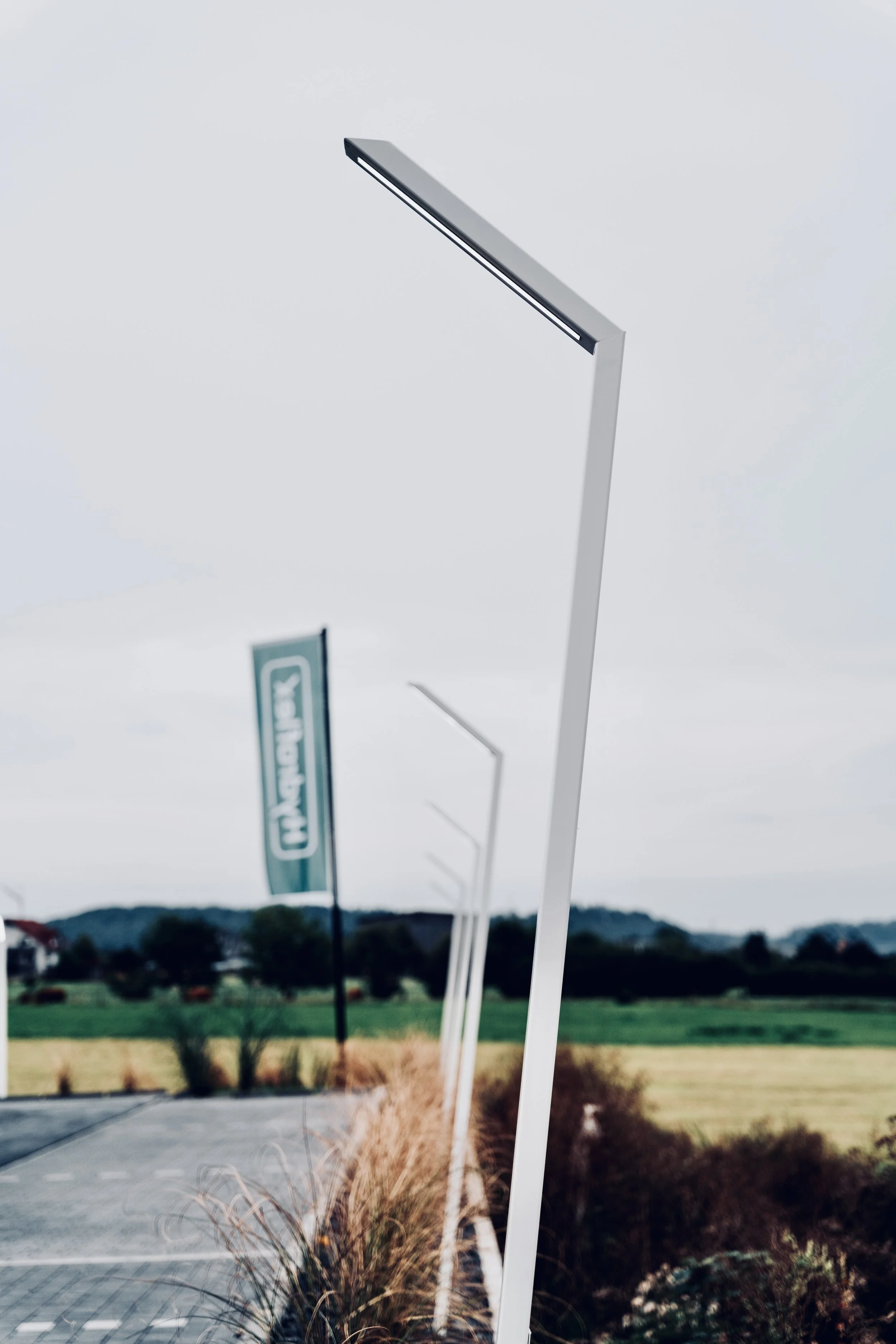 Blick auf ein fahles mittelgroßes Straßenschild an einem landwirtschaftlichen Feld, mit weiteren ähnlichen Schildern im Hintergrund, auf einer Straße im ländlichen Gebiet bei bewölktem Himmel.