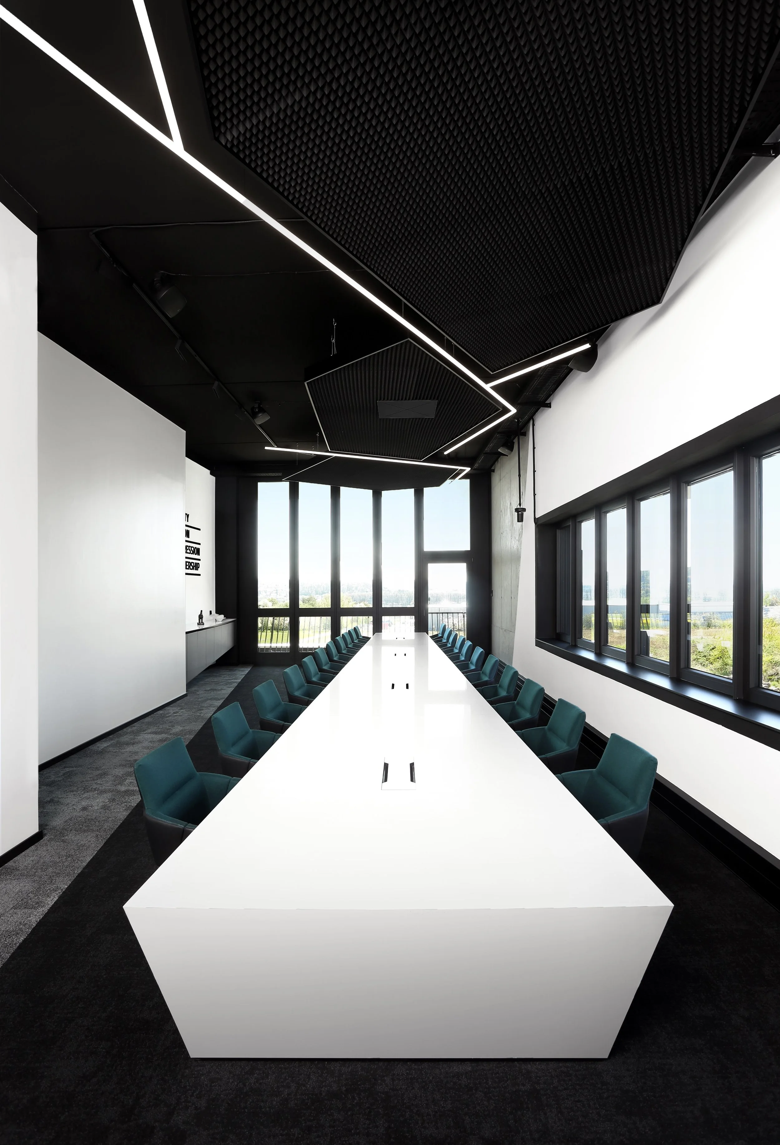 Moderner Konferenzraum mit weißem Tisch, grünen Stühlen, großen Fenstern und schallabsorbierenden schwarzen Deckenpanelen.
