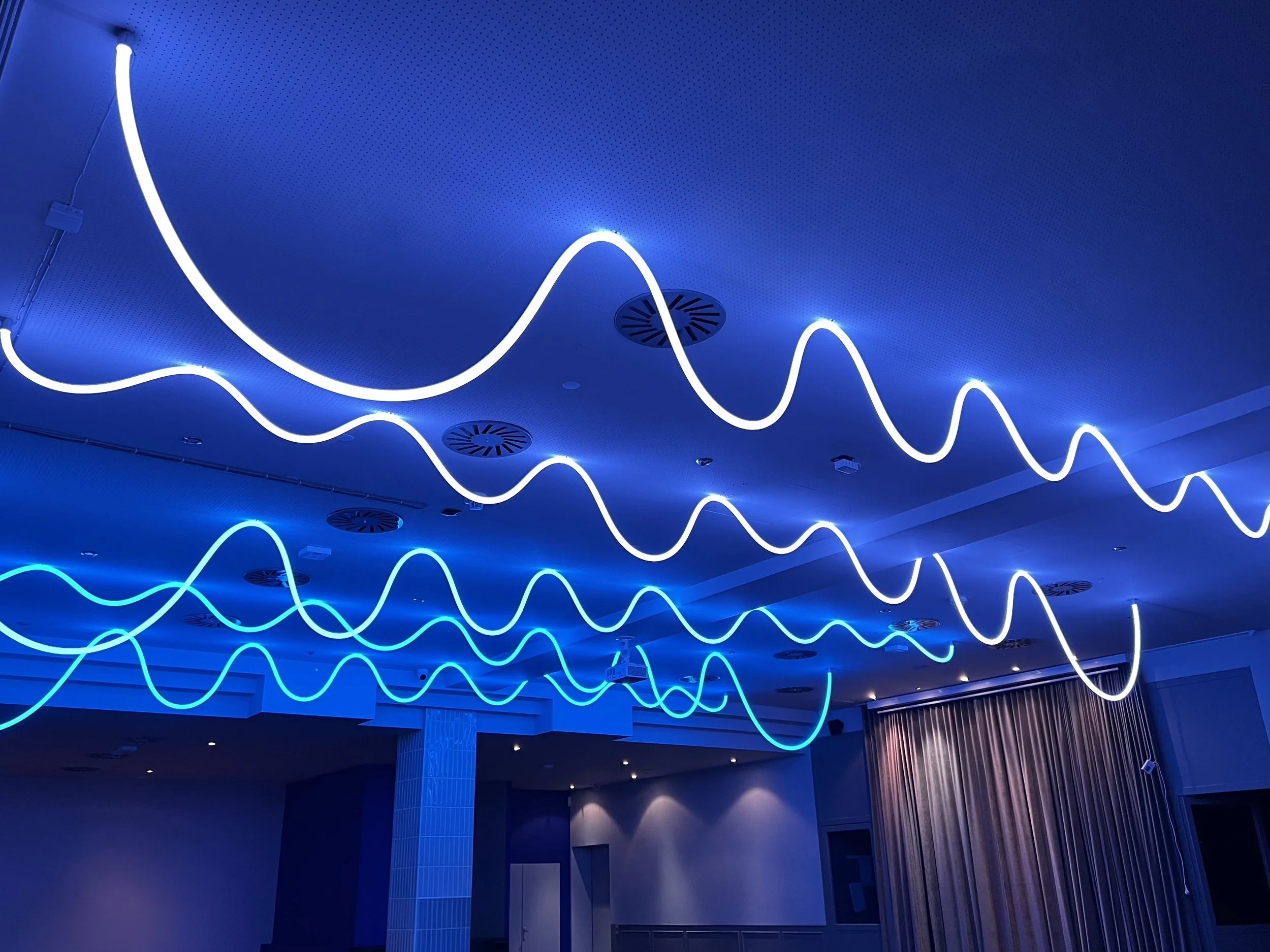 Blaue Deckenbeleuchtung in einem Raum, bestehend aus einer Wellenförmigen Neonlampe, die an der Decke installiert ist.