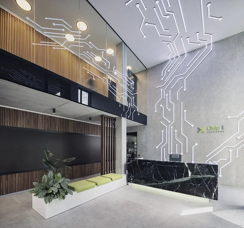 Moderne Empfangshalle mit grafischer LED-Deckenbeleuchtung, schwarzer Marmor-Frontdesk, Sitzbank mit grünen Kissen und Pflanzen, mit der Beschriftung 'Xchange' an der Wand.