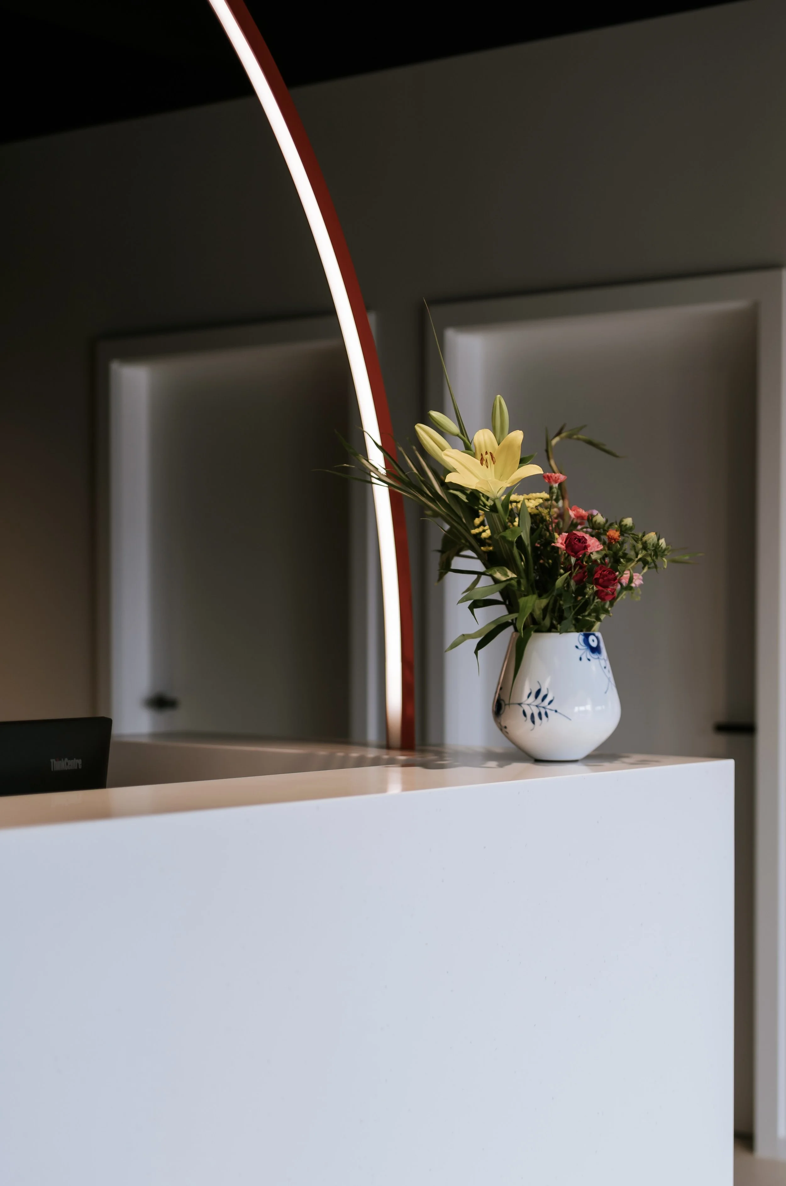 Blumenstrauß mit Lilien und Rosen in einer weißen Vase auf einem weißen Tresen, moderne Inneneinrichtung im Hintergrund und Lichtakzent.