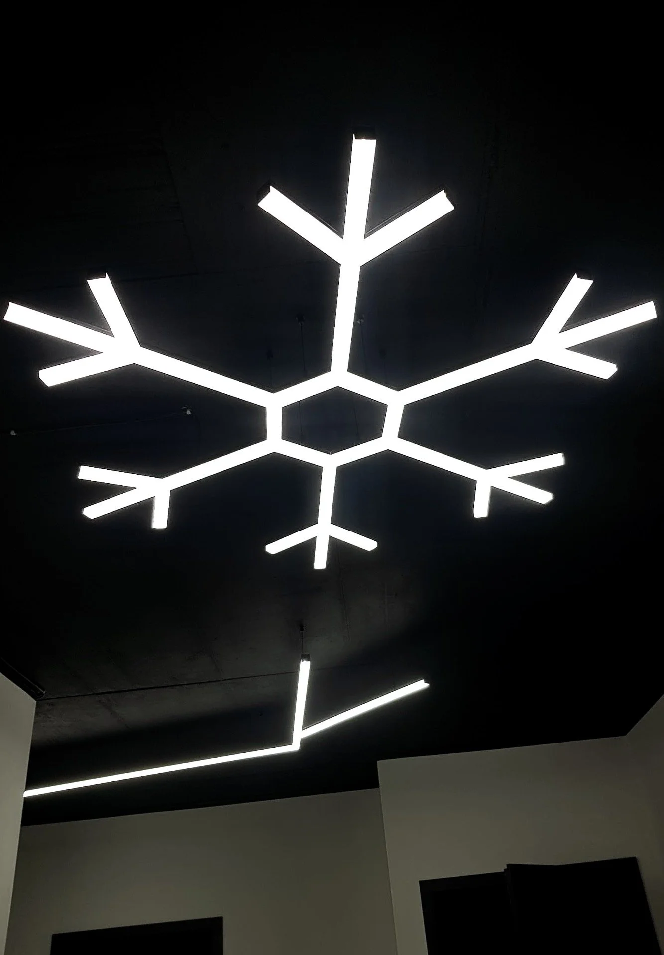 Moderne Beleuchtung in Form von leuchtenden Schneeflocken an der Decke in einem dunklen Raum.