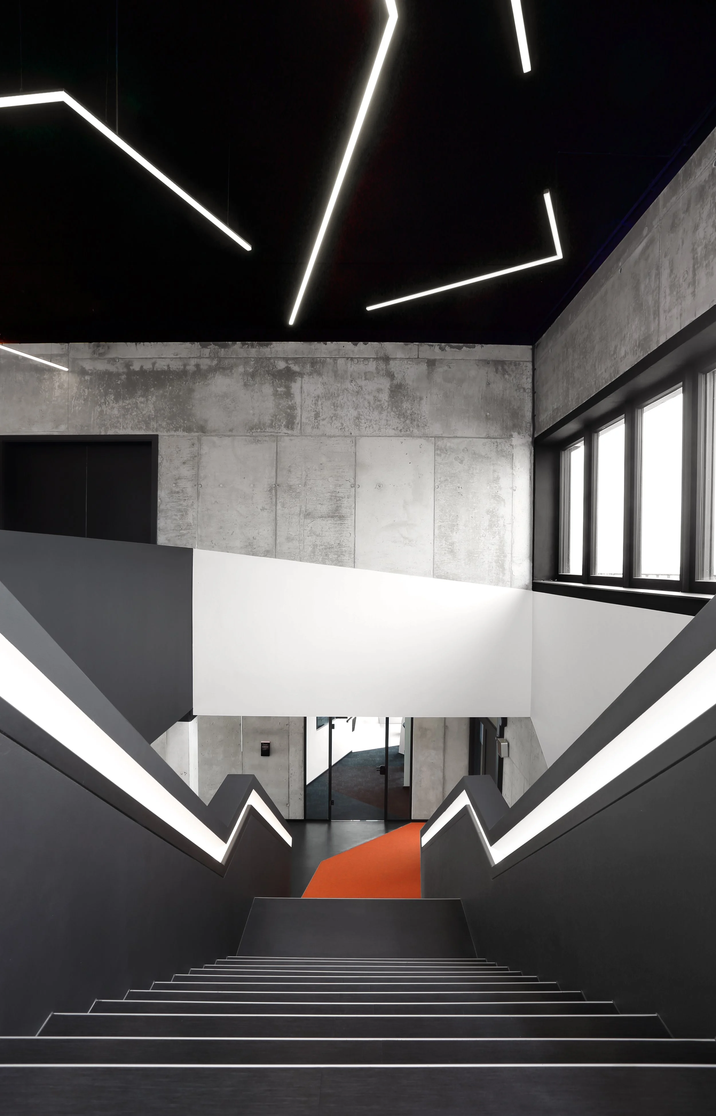 Innenansicht eines modernen Gebäudes mit Treppen und LED-Beleuchtung, Betonwänden und großen Fenstern.