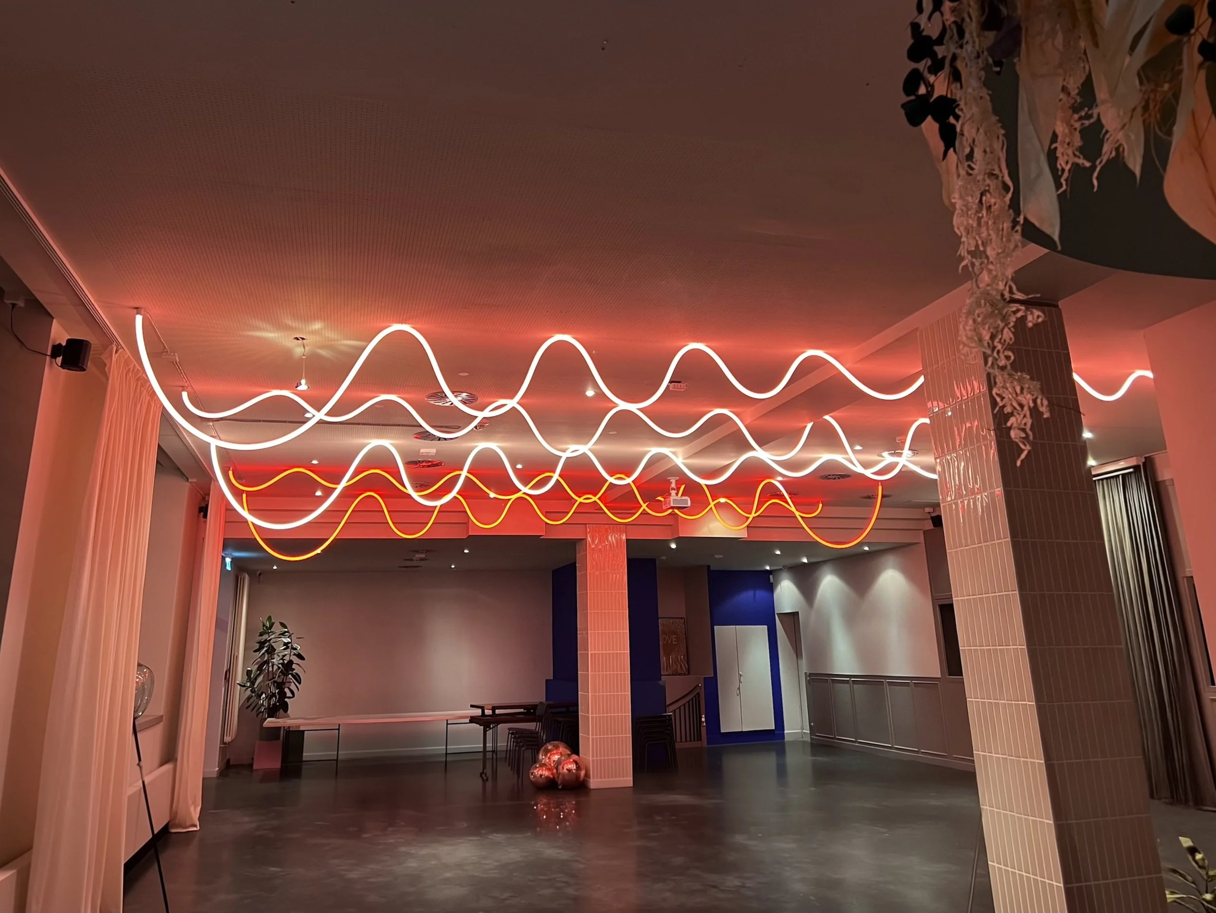 Dekorativer Raum mit leuchtenden weißen und roten dünnen Neon-Ästen an der Decke, große Pflanzen und dekorative Gegenstände auf dem Boden.