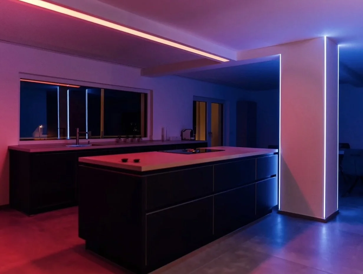 Moderne Küche bei Nacht mit buntem LED-Beleuchtung, dunklen Schränken und großen Fenstern