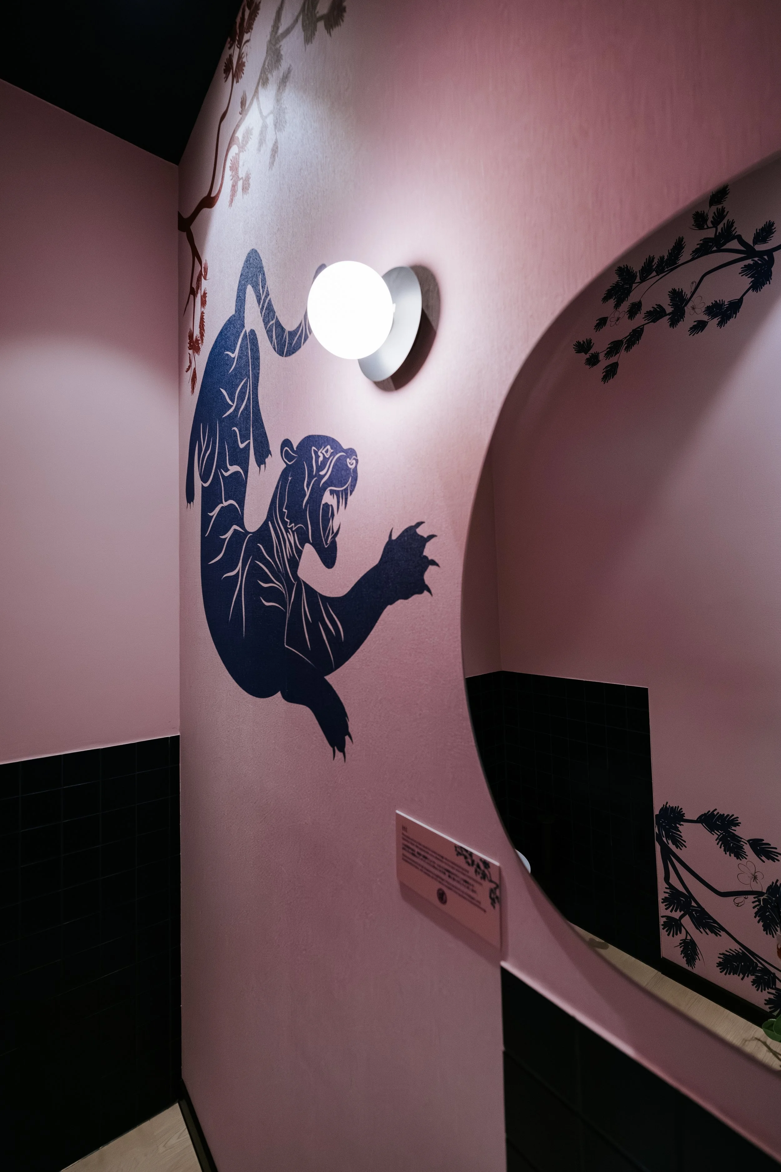 Eine Wand mit grünen und blauen Tierzeichnungen, ein Wandlicht und eine Karte mit QR-Code