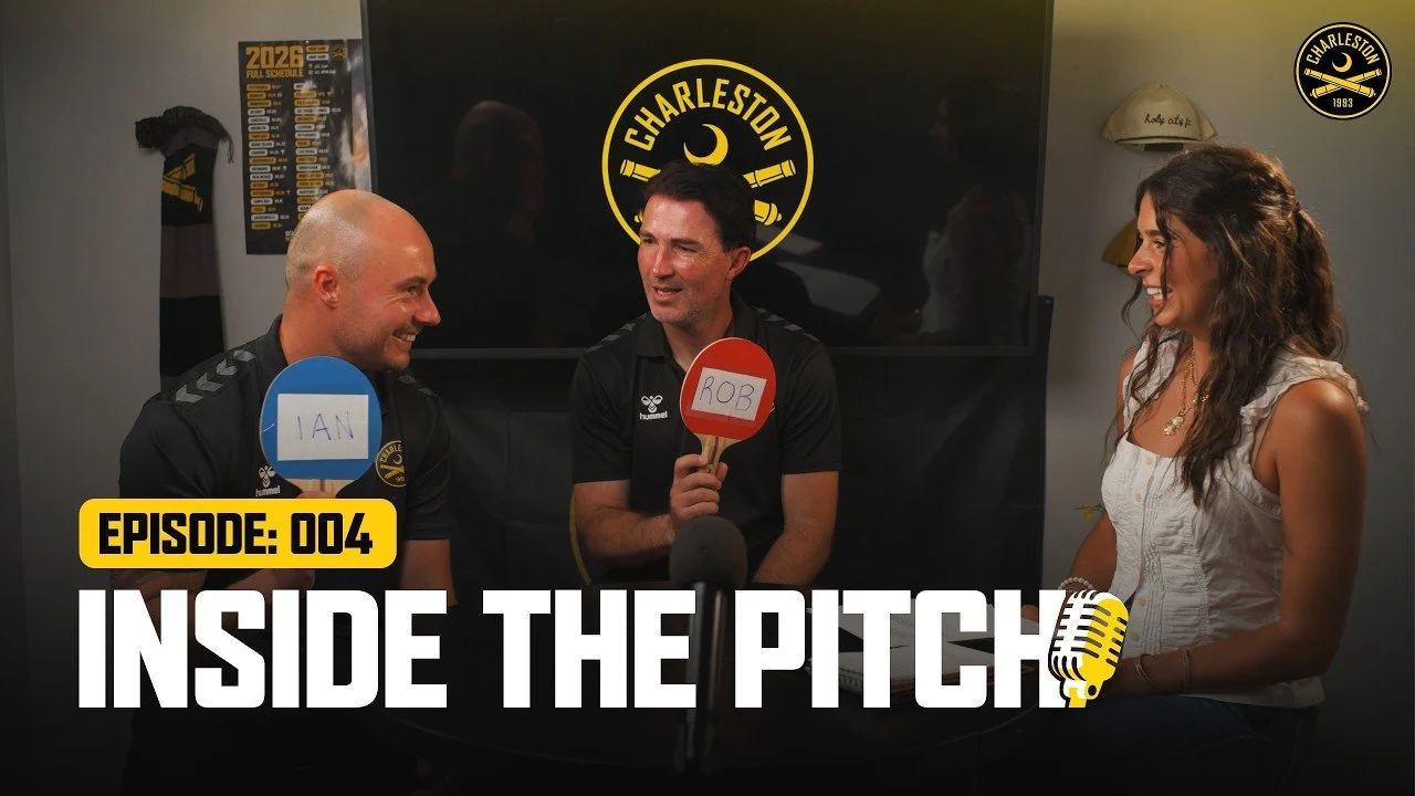 Three people sitting at a table during an interview, holding paddles with names 'Ian', 'Rob', and an unidentified person, with the 'Charleston' logo in the background, and a woman smiling on the right.