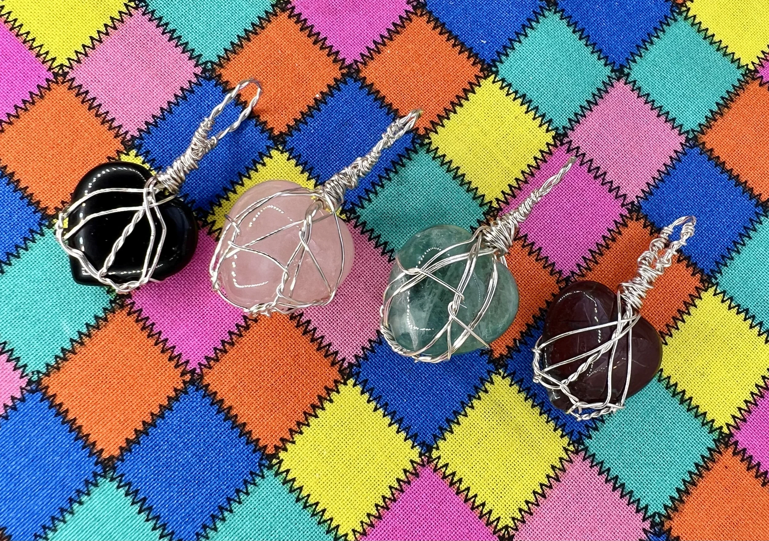 Colorful fabric with a diamond pattern in bright pink, blue, yellow, orange, and teal, featuring black zigzag outlines and several wire-wrapped stones on top.