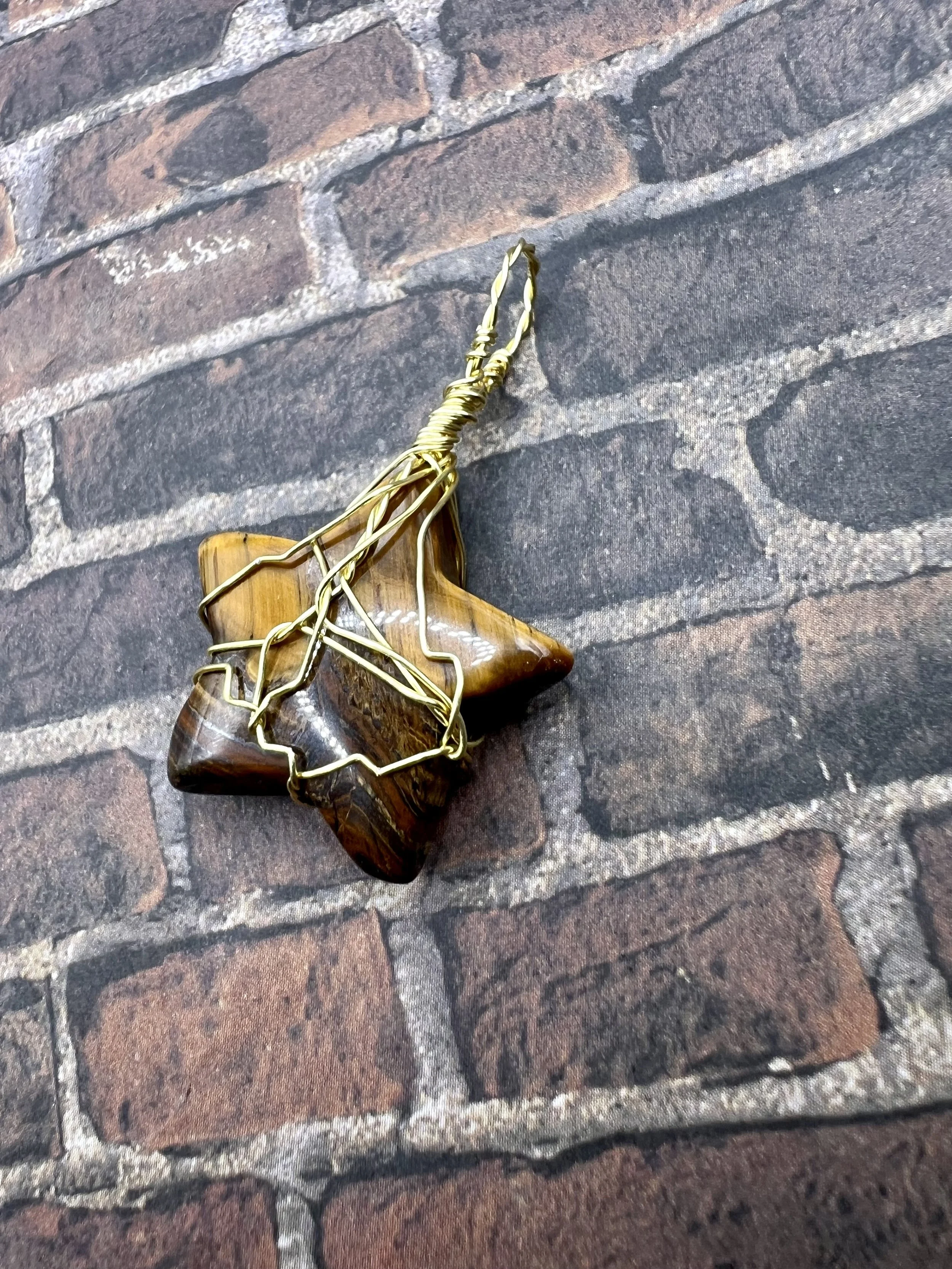 A decorative object resembling a star made of polished brown stone with gold-colored wire outlining its shape, lying on a textured brick surface.