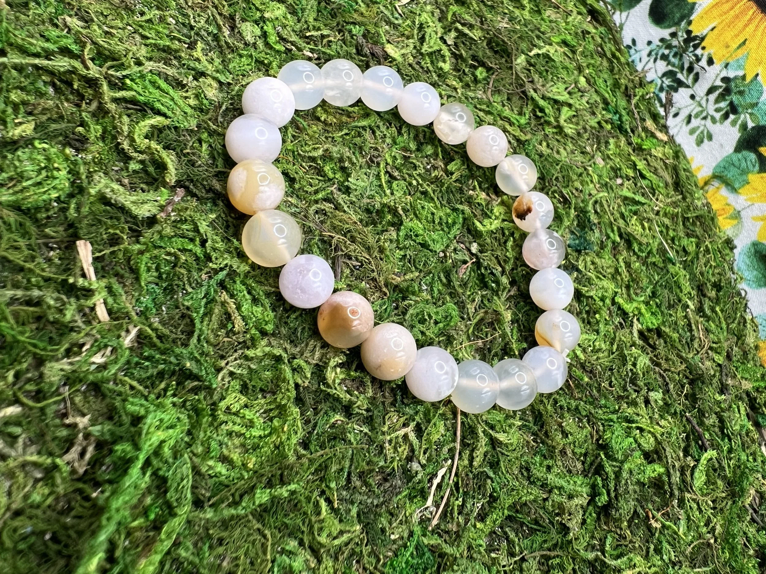A string of white and light-colored beads arranged in a circle on a vibrant green mossy surface with a portion of fabric with a floral pattern visible on the right side.