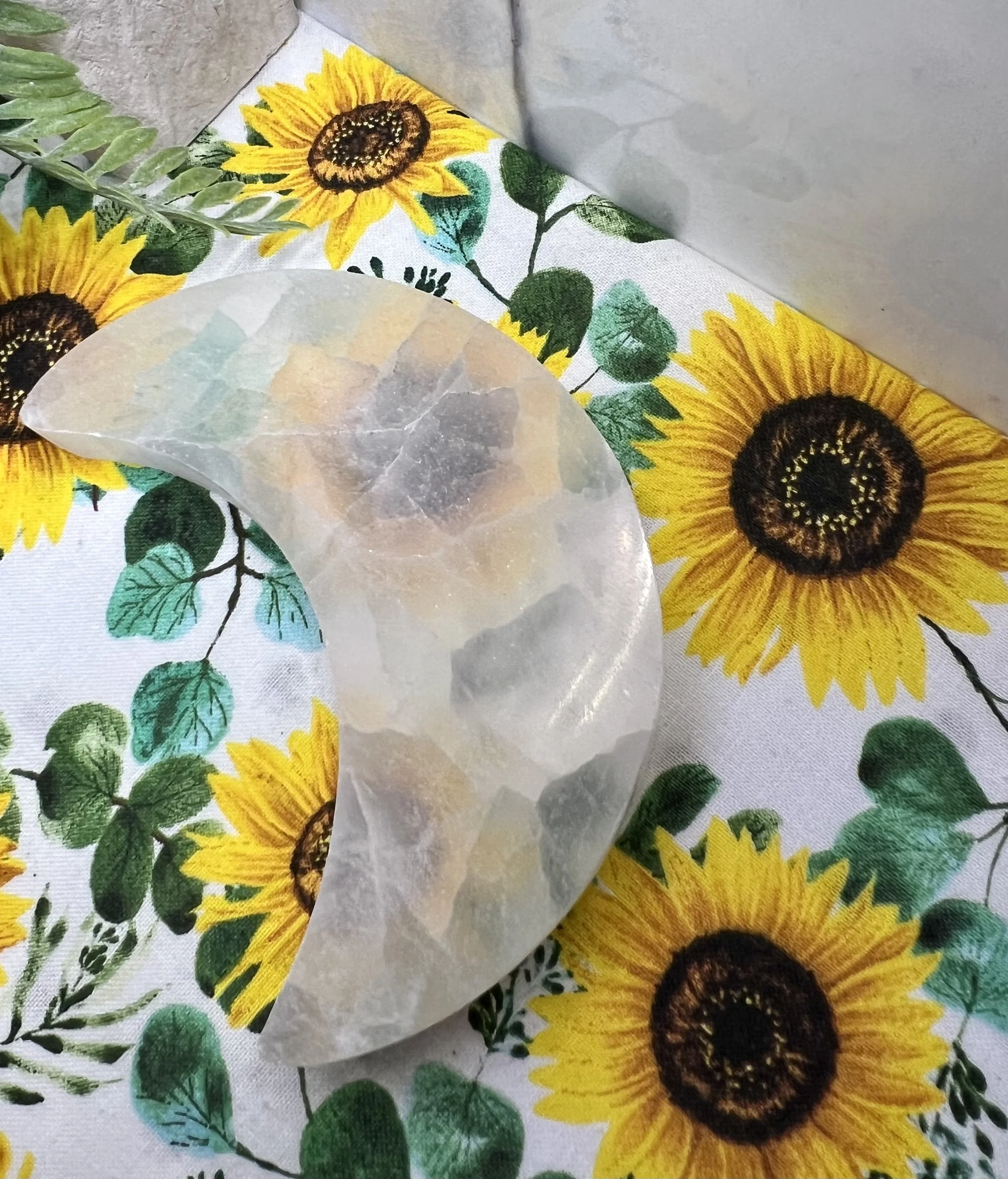 Close-up of a decorative amber or quartz crystal on a sunflower-patterned fabric, with yellow sunflowers and green leaves.