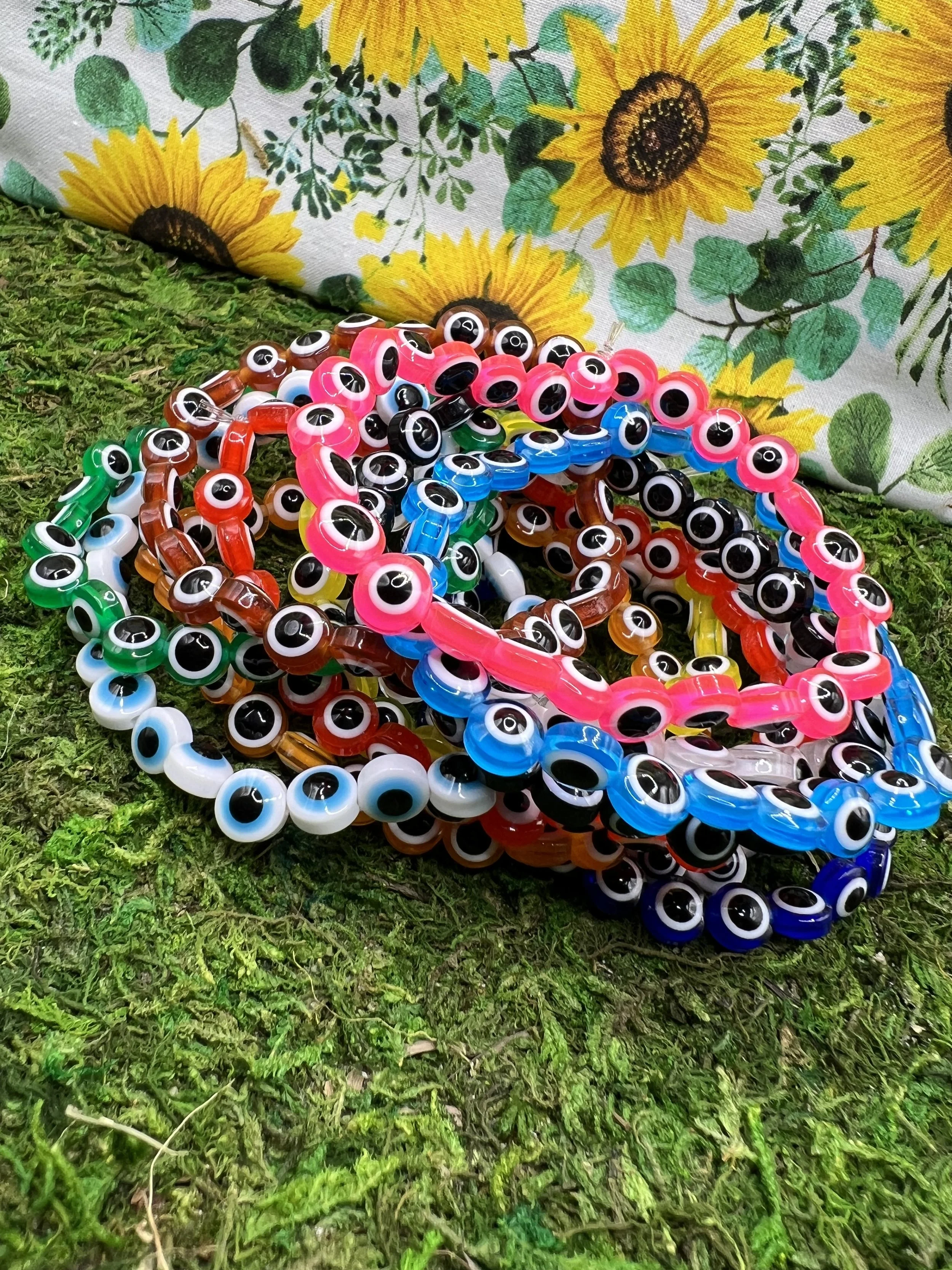 Colorful plastic eyeball necklaces spread on green grass with a sunflower-patterned cloth in the background.