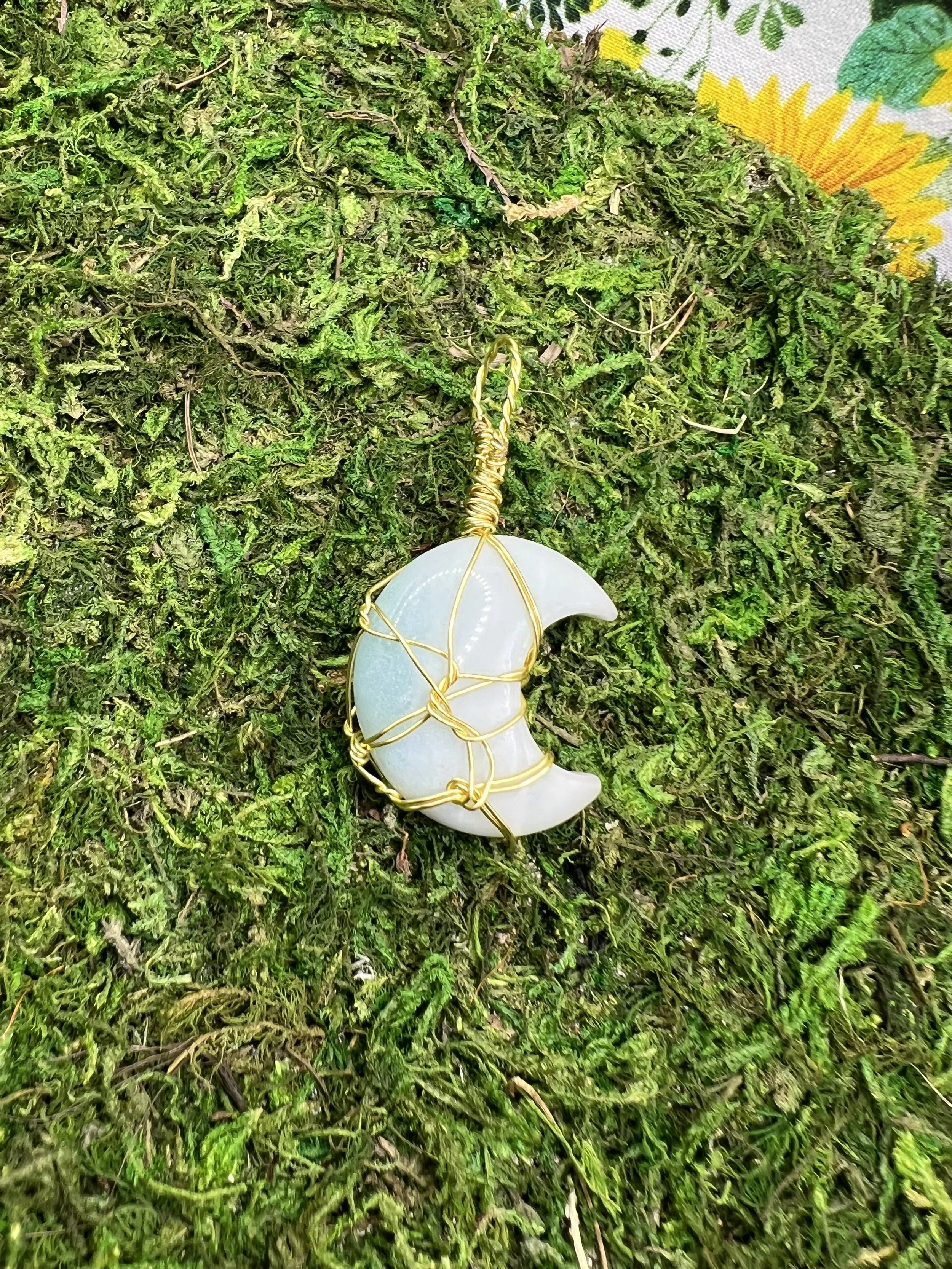 A moon-shaped pendant wrapped in gold wire resting on green moss.