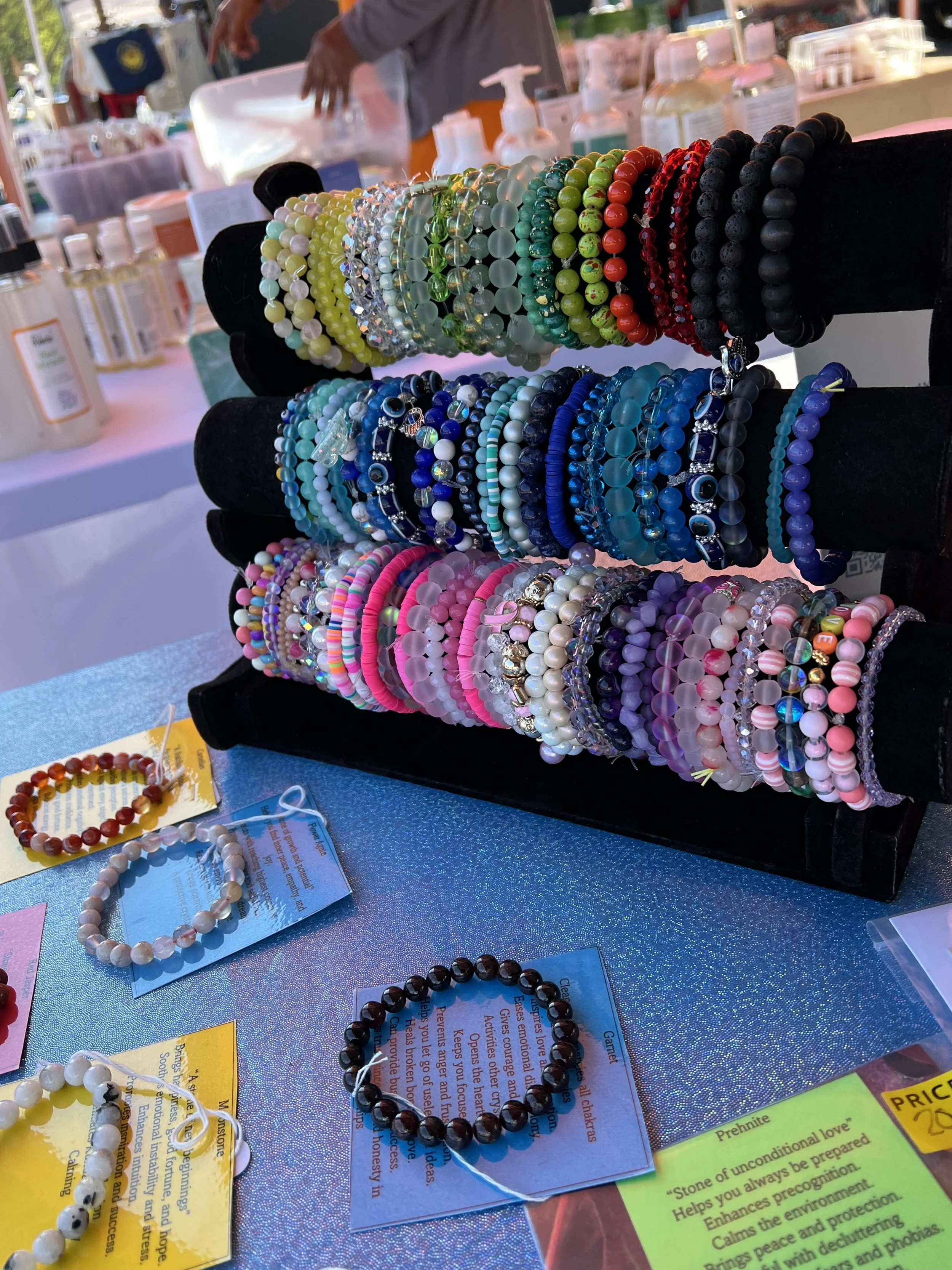 Display of various colorful beaded bracelets at a market stall with informational and price tags.
