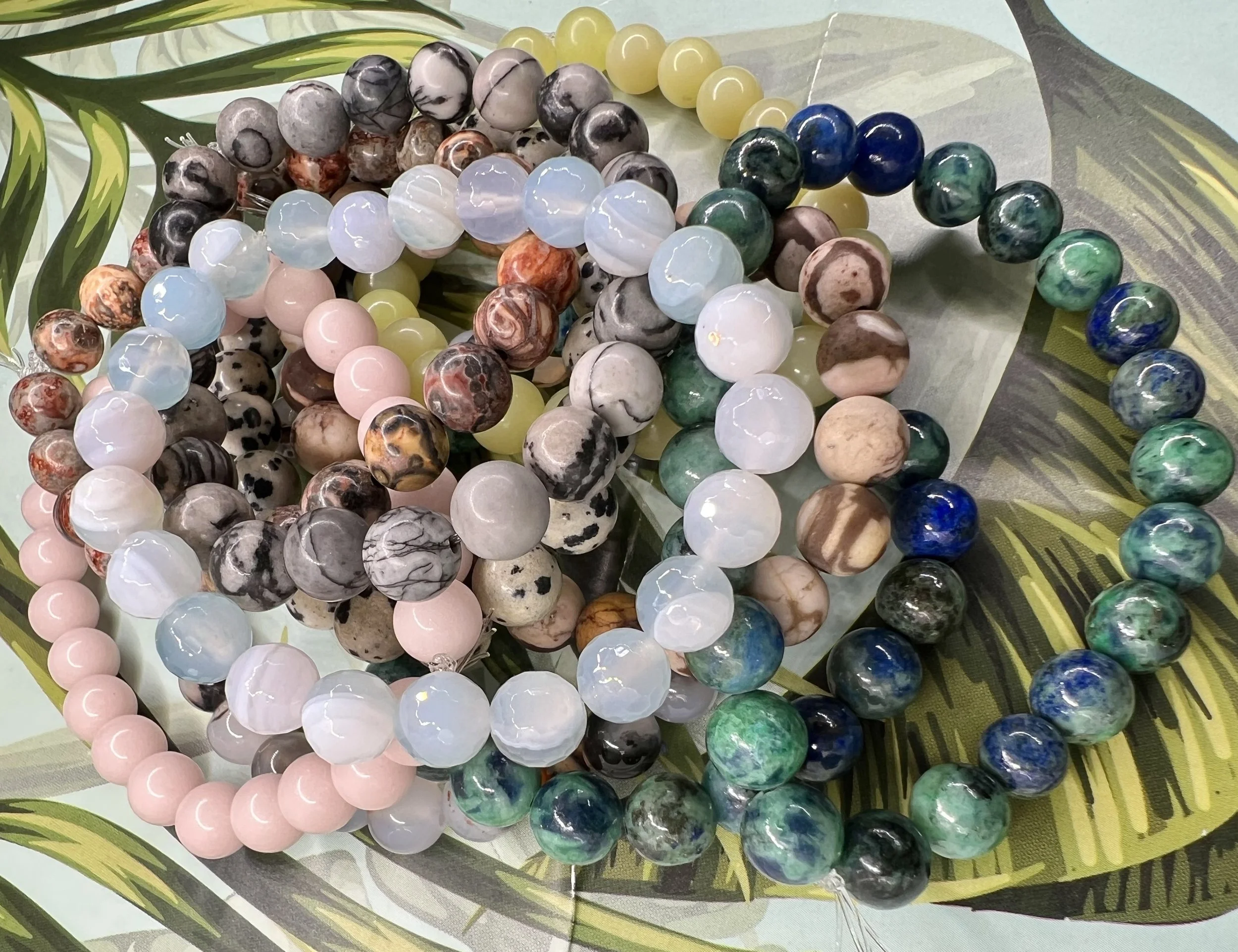 Several strands of colorful round beads arranged on a piece of patterned fabric with a green leaf nearby.