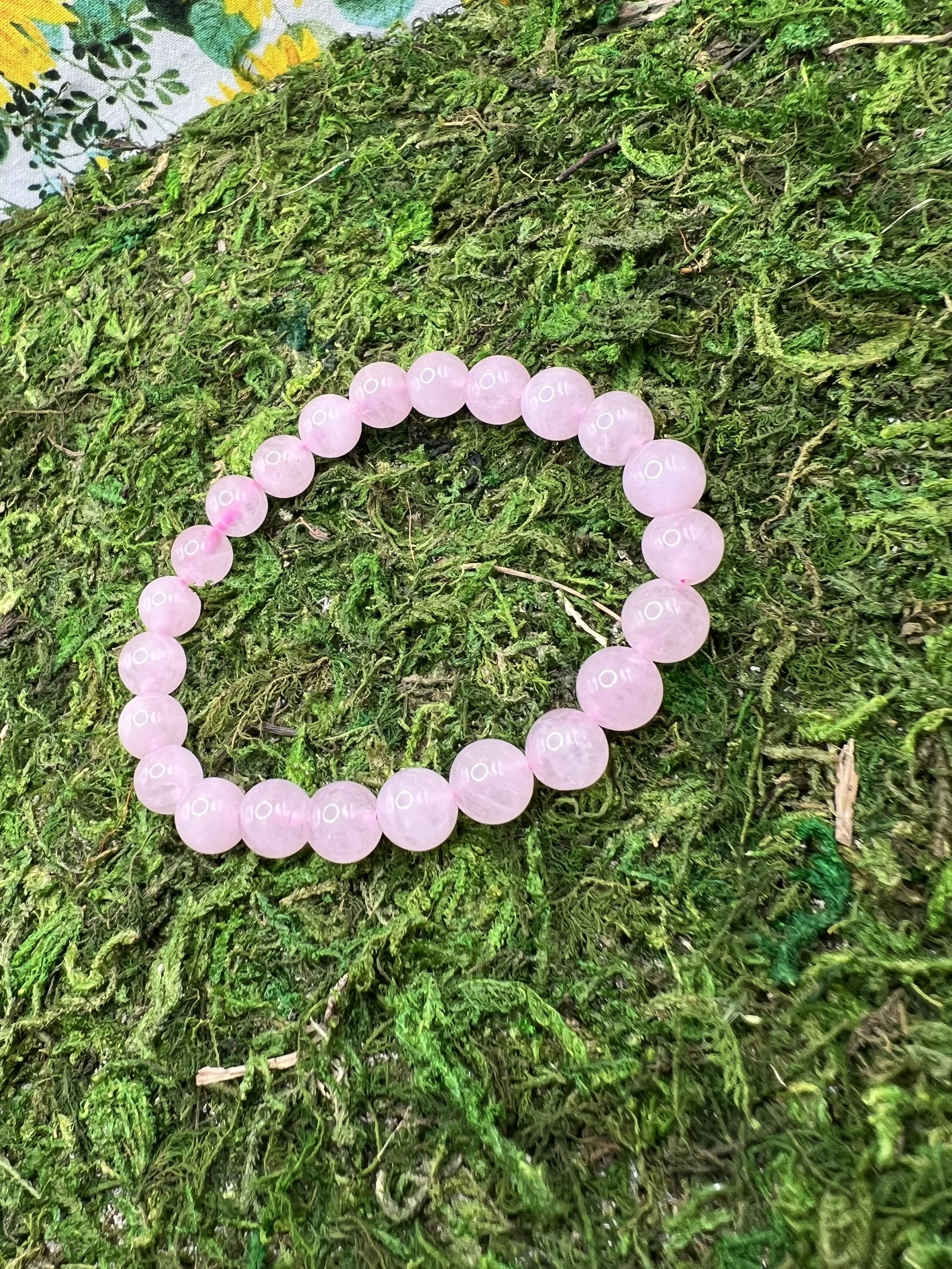 A pink beaded bracelet resting on green moss and foliage.