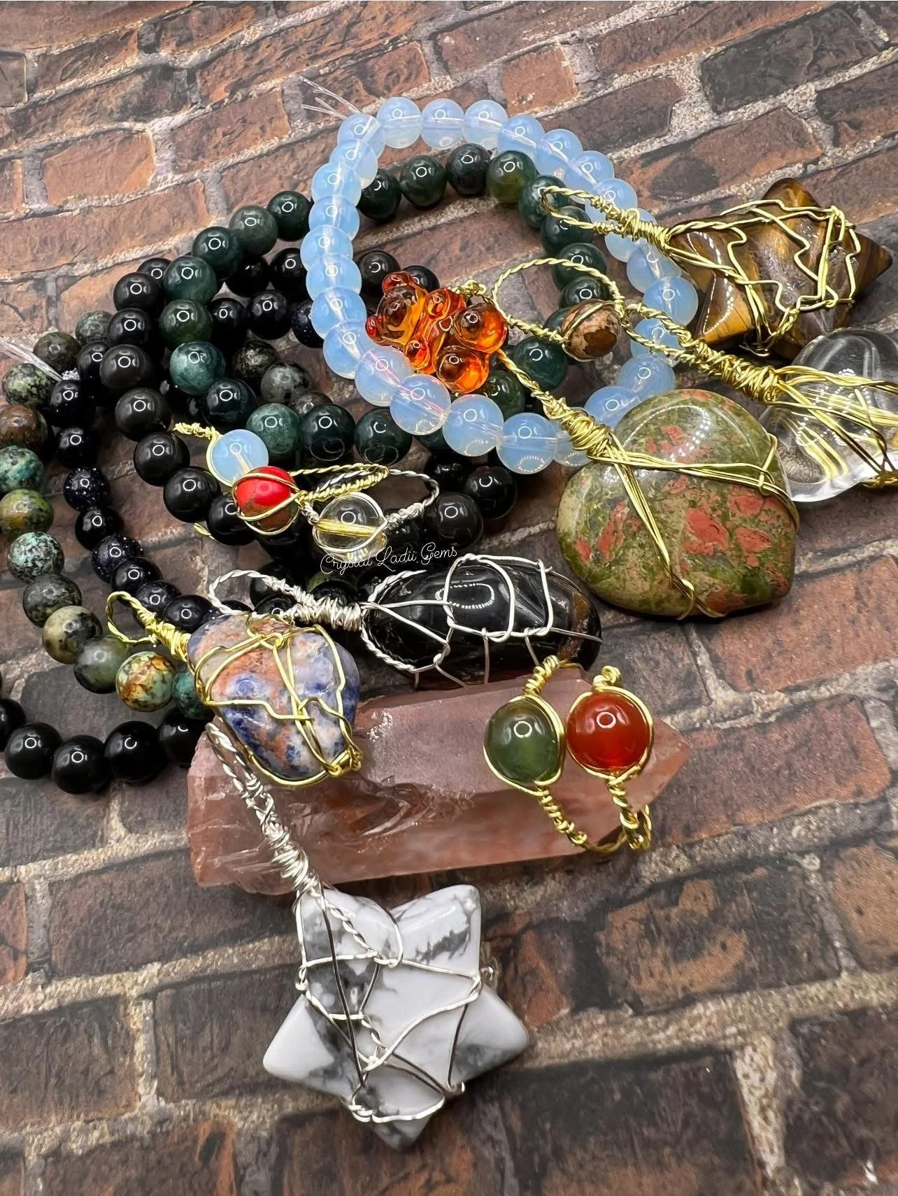 Assorted beaded jewelry and wire-wrapped stones on a brick surface, including necklaces and bracelets with colorful and semi-precious stones.