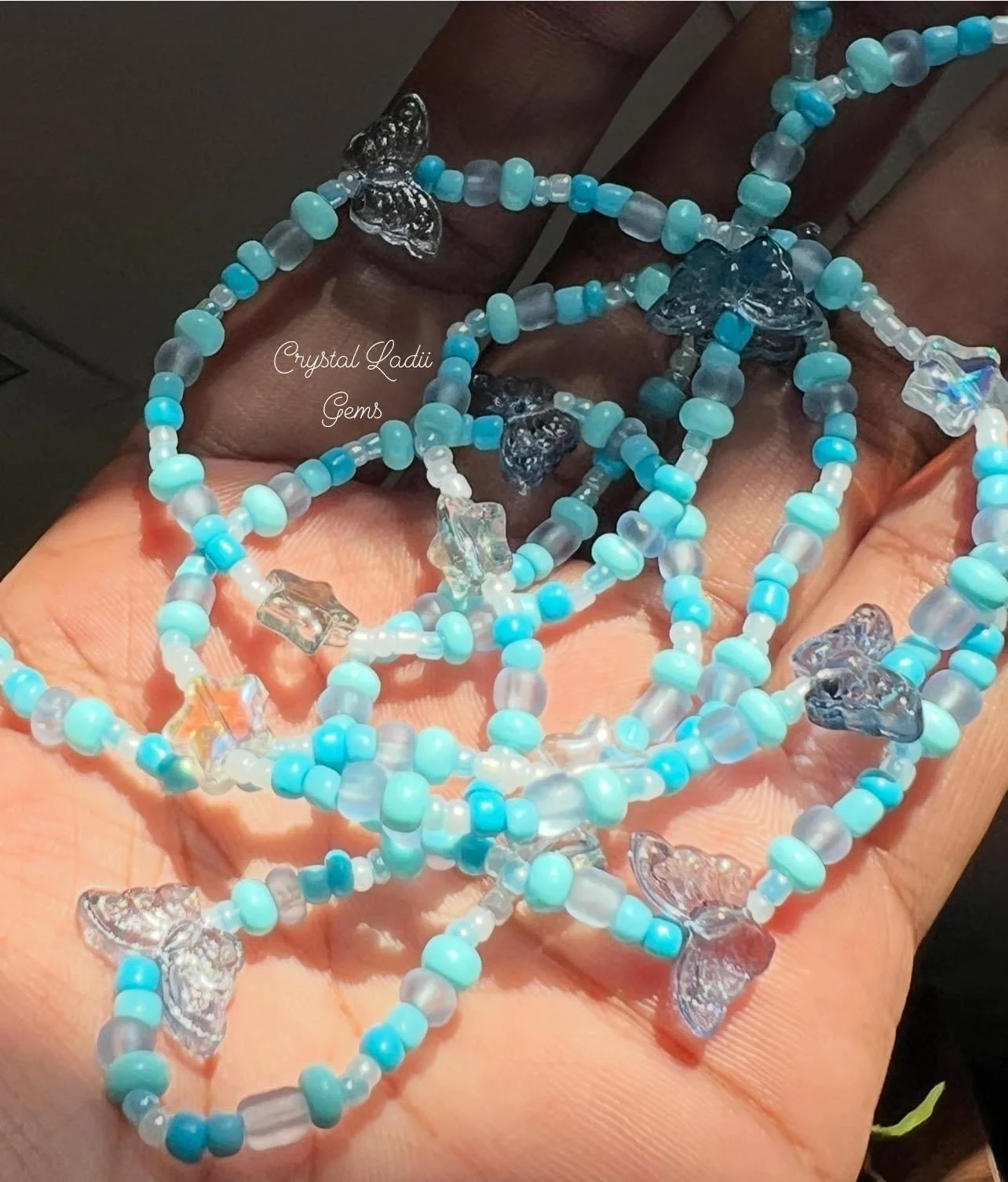 Close-up of a hand holding multiple blue and clear beaded necklaces with butterfly-shaped charms.