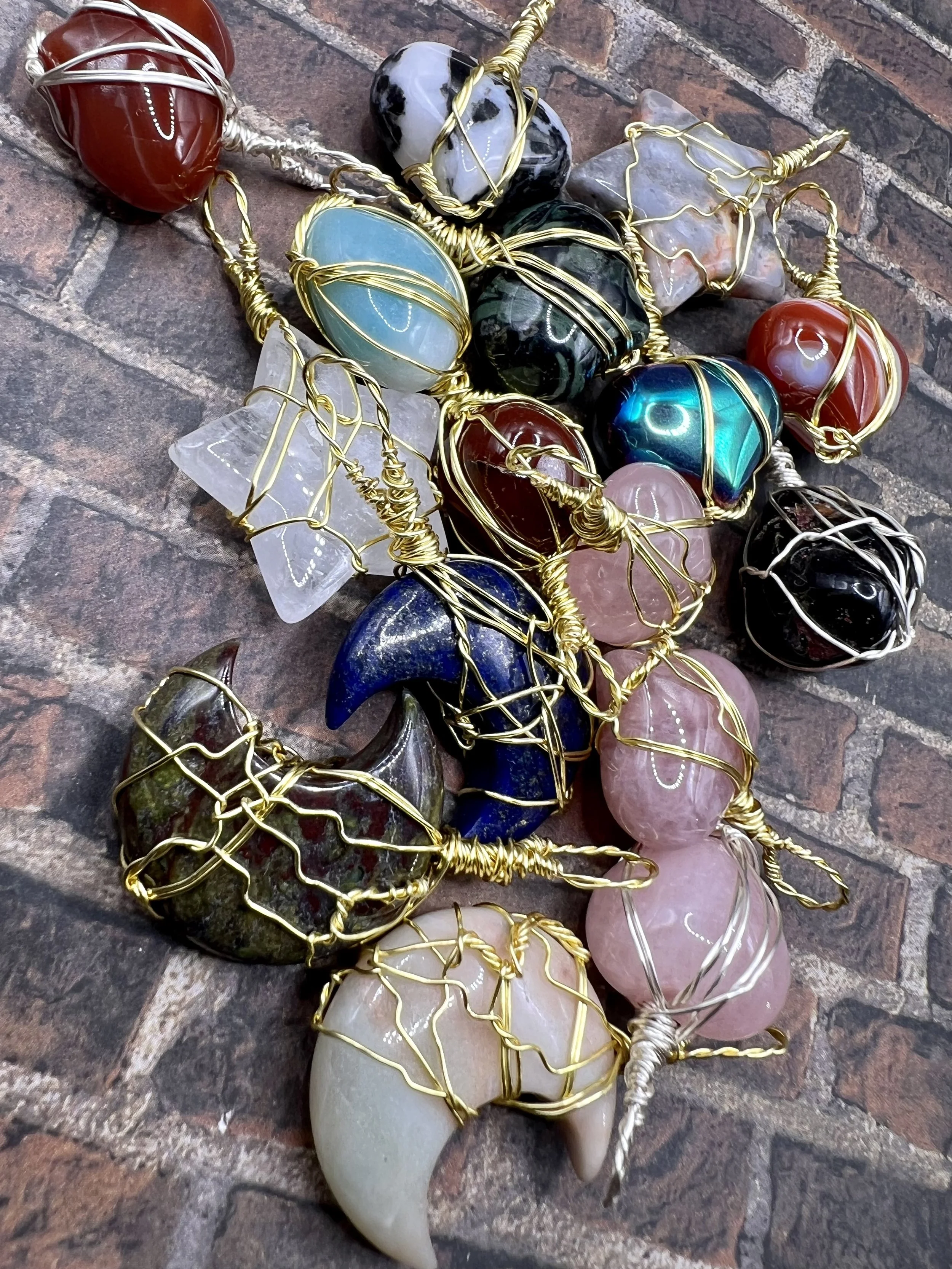 Various polished stones wrapped in wire, placed on a brick surface, resembling angel or fairy figures.
