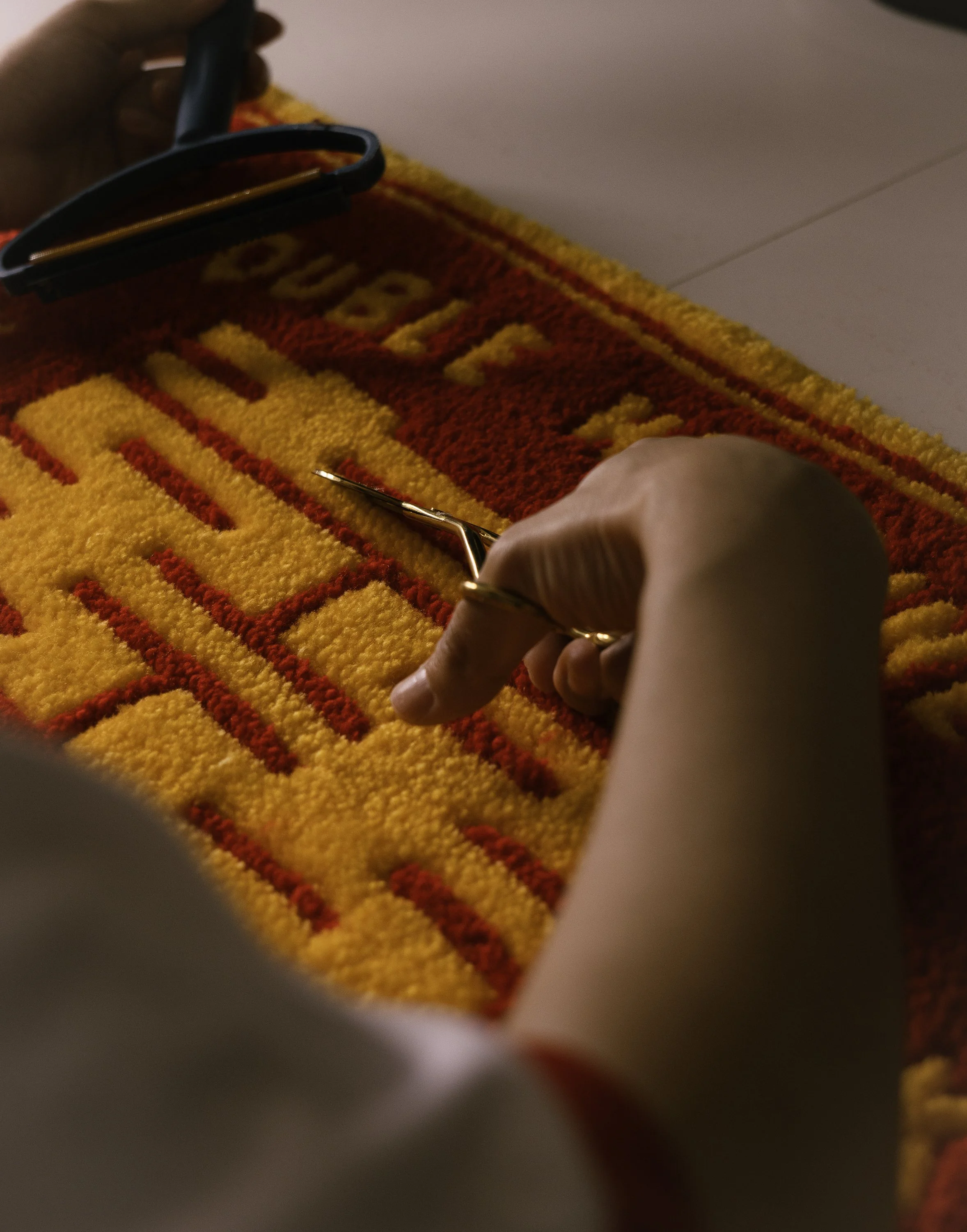 A person using tweezers to pick or arrange small red objects on a colorful, patterned textile with yellow and red colors.