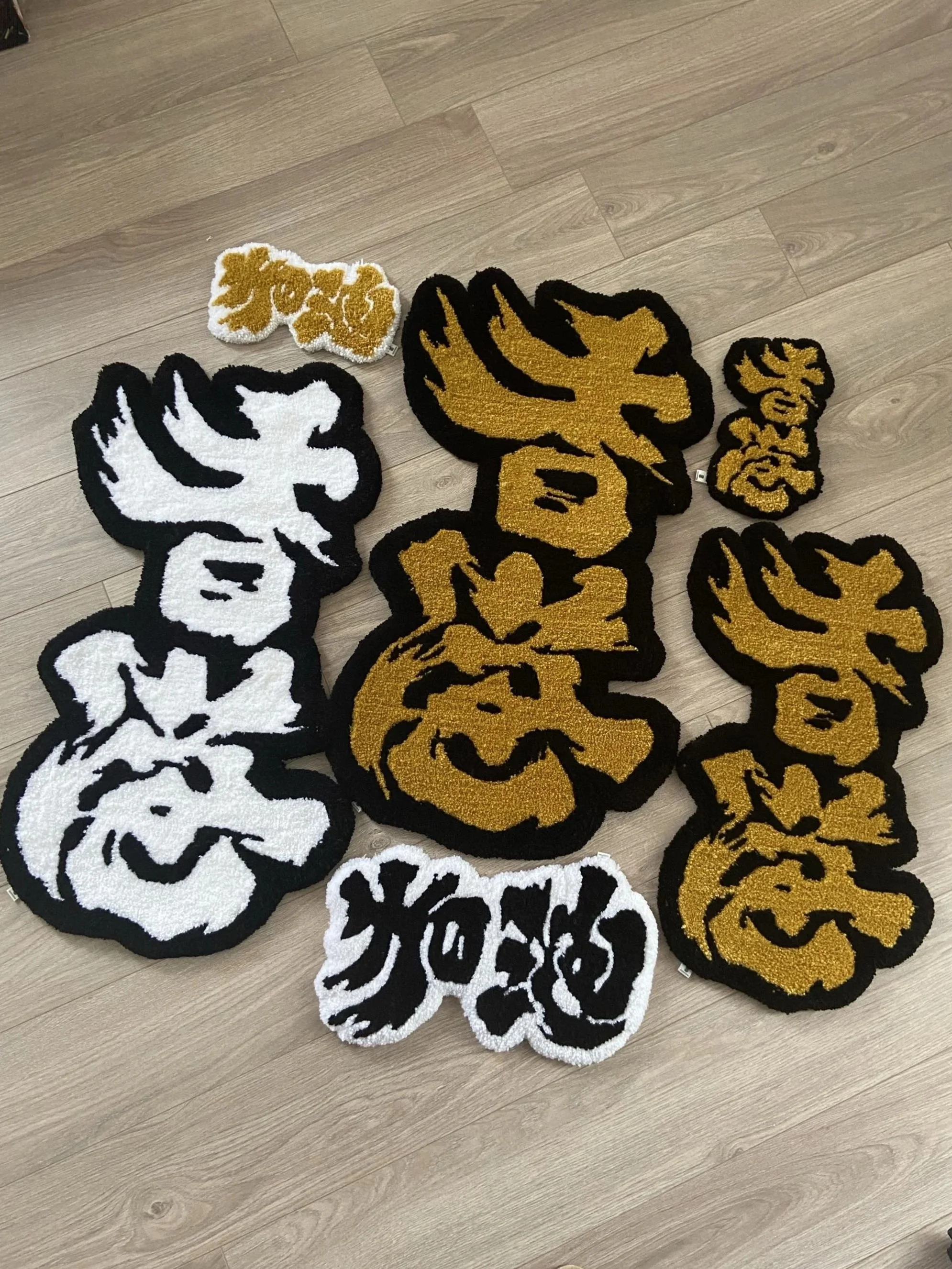Floor rugs with Chinese calligraphy  in black, white, and gold colors arranged on a wooden floor.