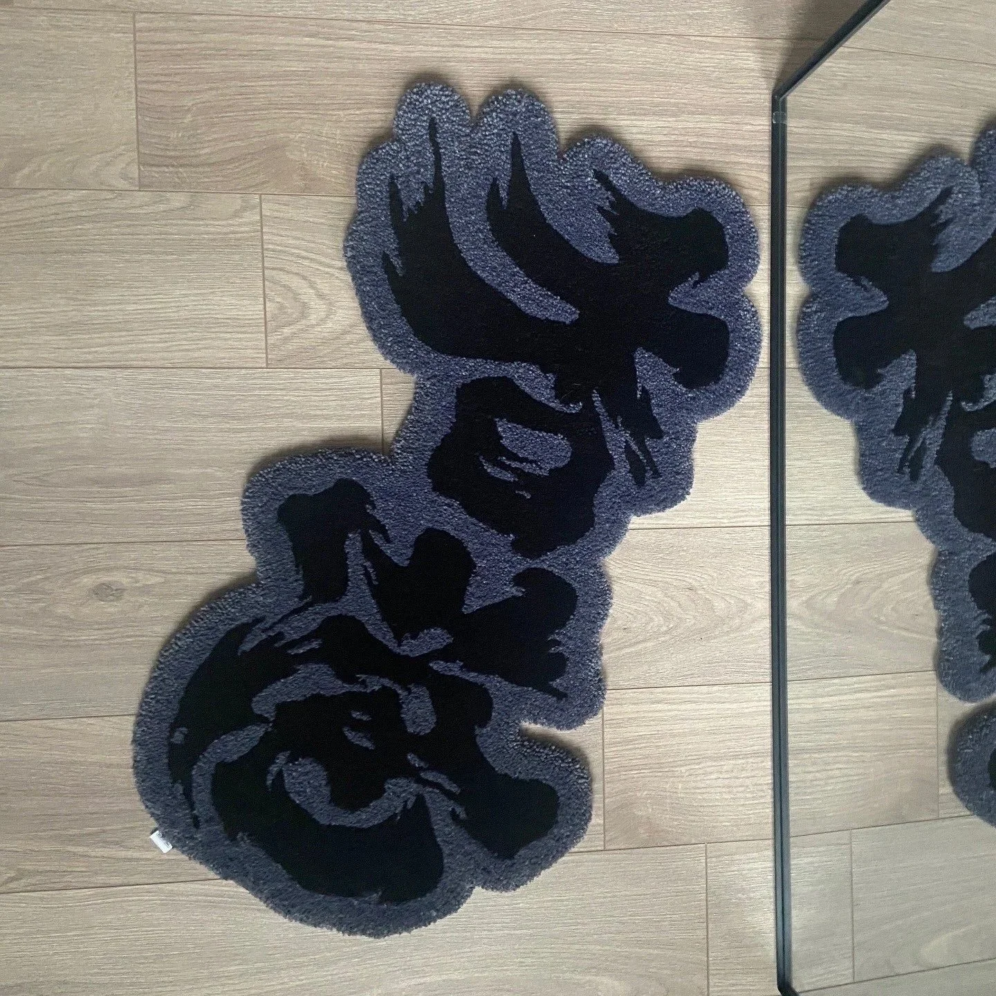 Black and gray Chinese calligraphy rug with abstract floral pattern on a wooden floor, next to a mirror.