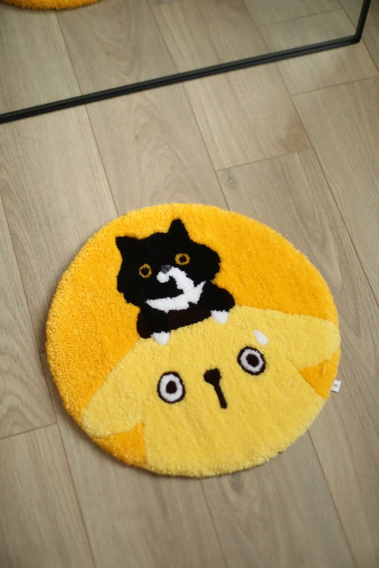 Round yellow rug with a black cat design and black and white eyes, nose, and whiskers, on a wooden floor.