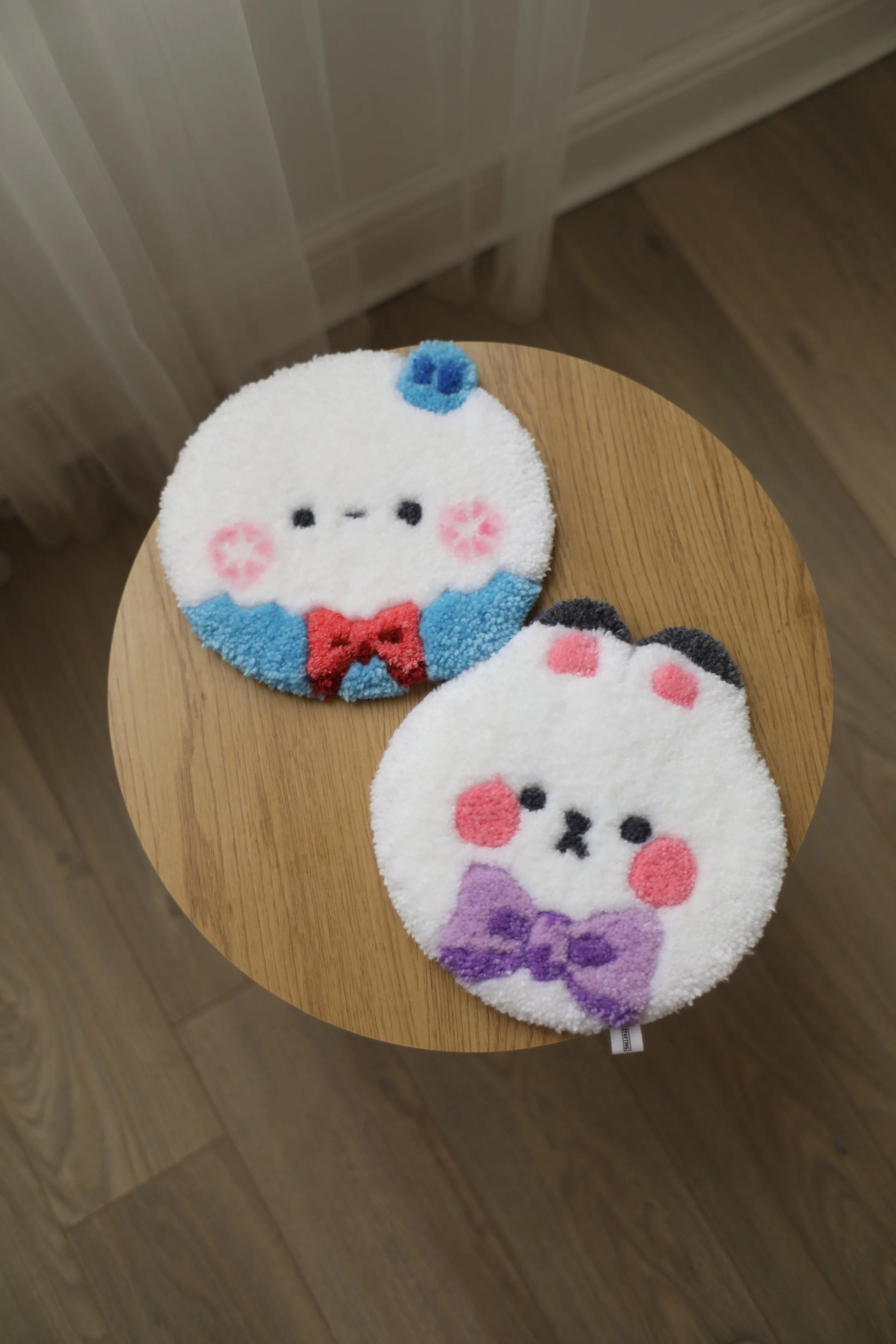 Two circular plush towels with cartoon faces, pink cheeks, and bows, placed on a wooden table.