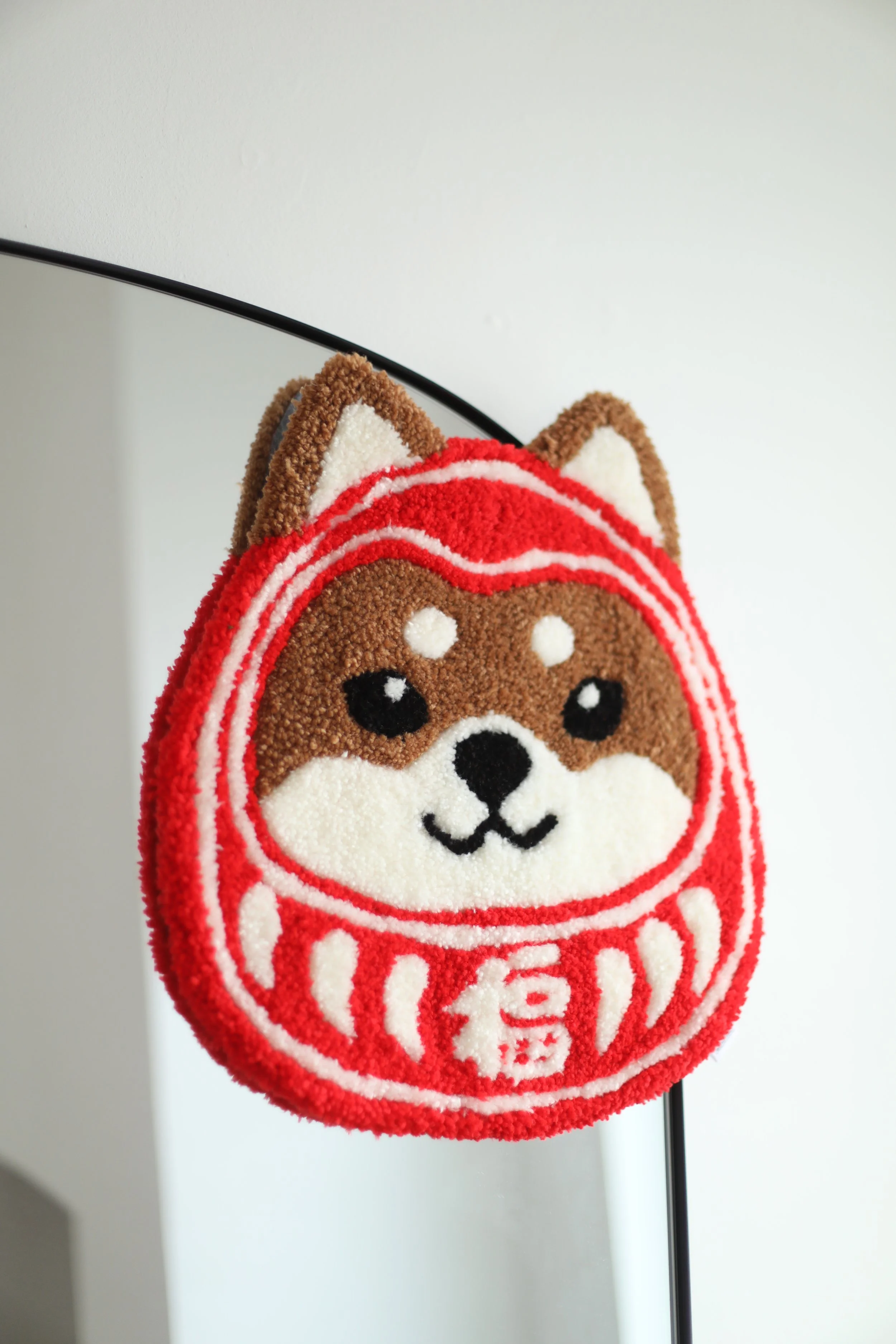 A decorative rug of a dog's face, specifically a Shiba Inu, designed to look like a traditional Japanese Daruma doll, with a red and white pattern.