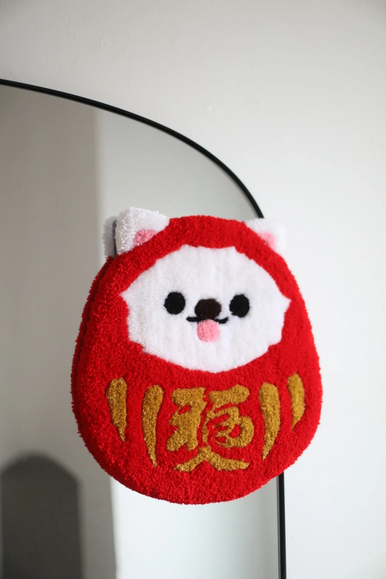 Red decoration rug in the shape of a Daruma doll with a cute dog face, black eyes, and pink tongue, featuring Japanese characters in gold on the front.