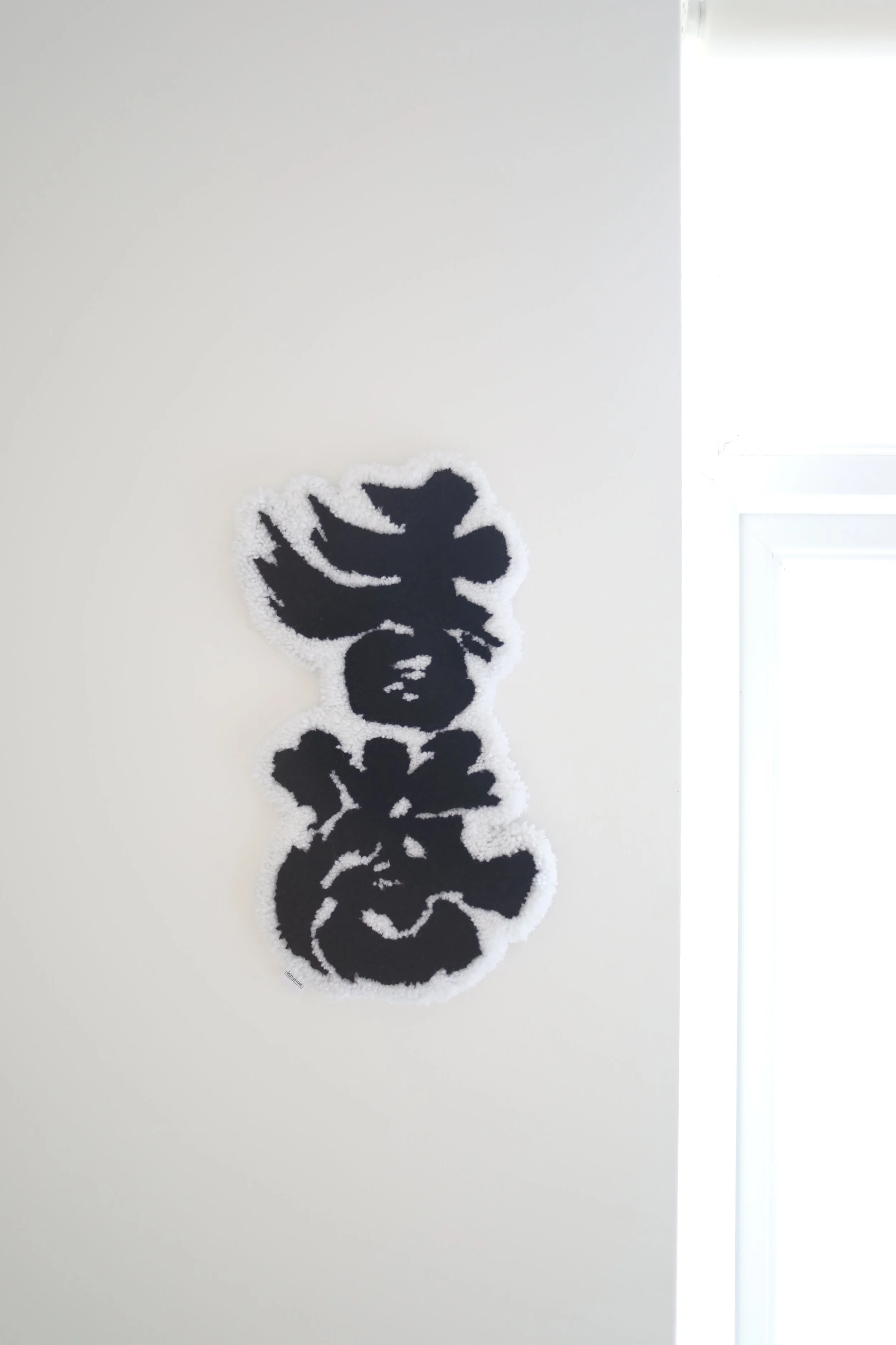 Black and white  Chinese calligraphy rug, hanging on a white wall near a window.