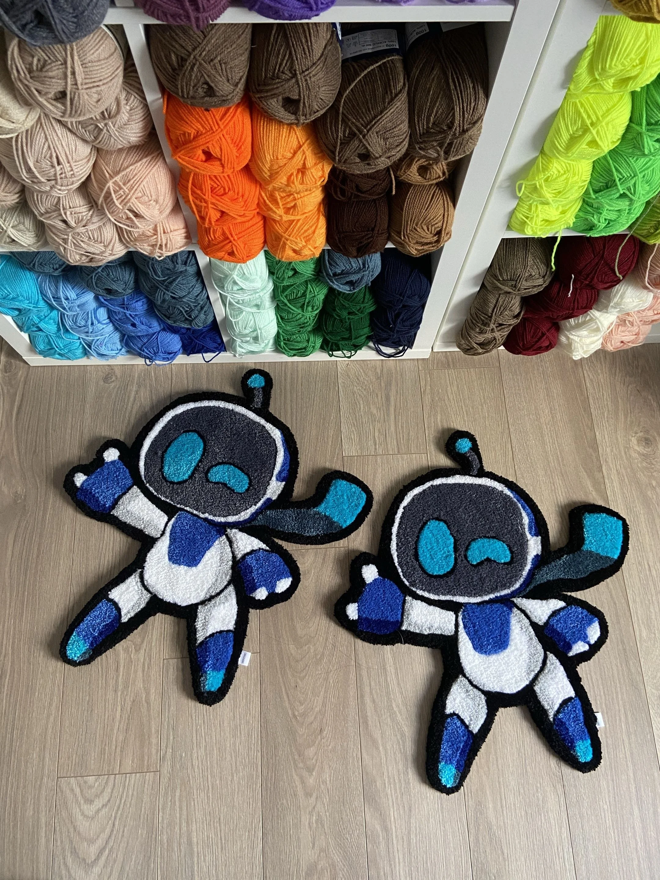 Colorful yarn balls on white storage shelves and two cartoon-style animal-shaped rugs on wooden floor.