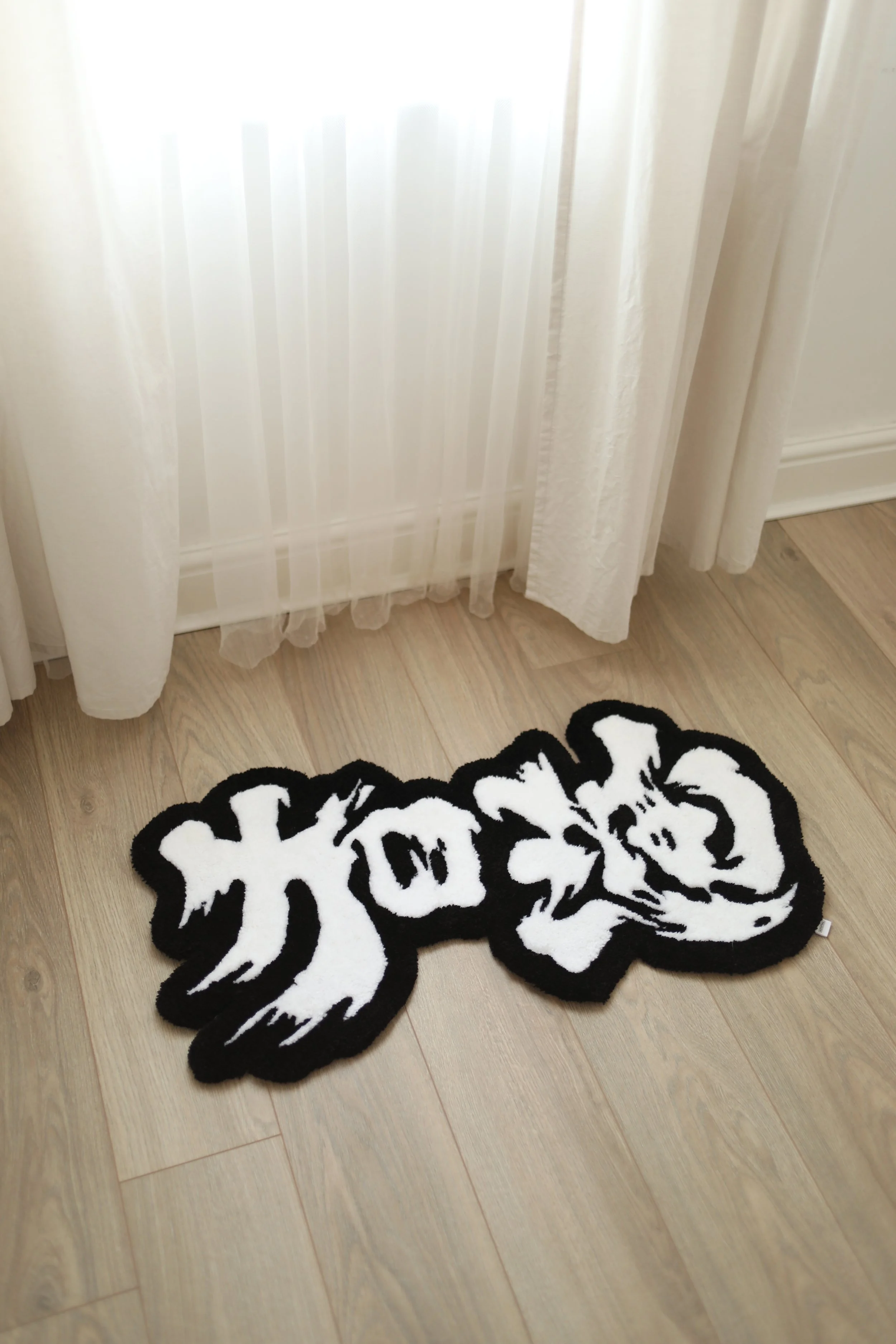 Floor rug with Chinese calligraphy in black and white on a wooden floor near white curtains.