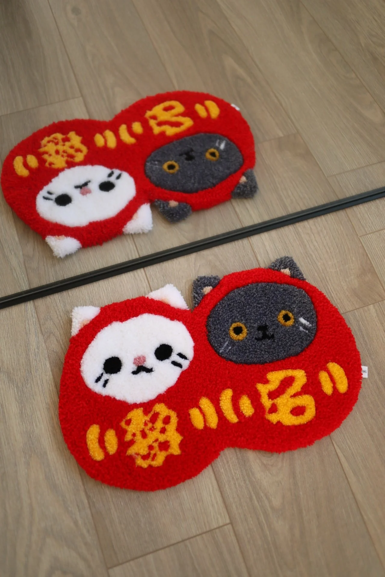 Red rug with cute cat faces daruma and Chinese characters, reflected in a mirror on a wooden floor.