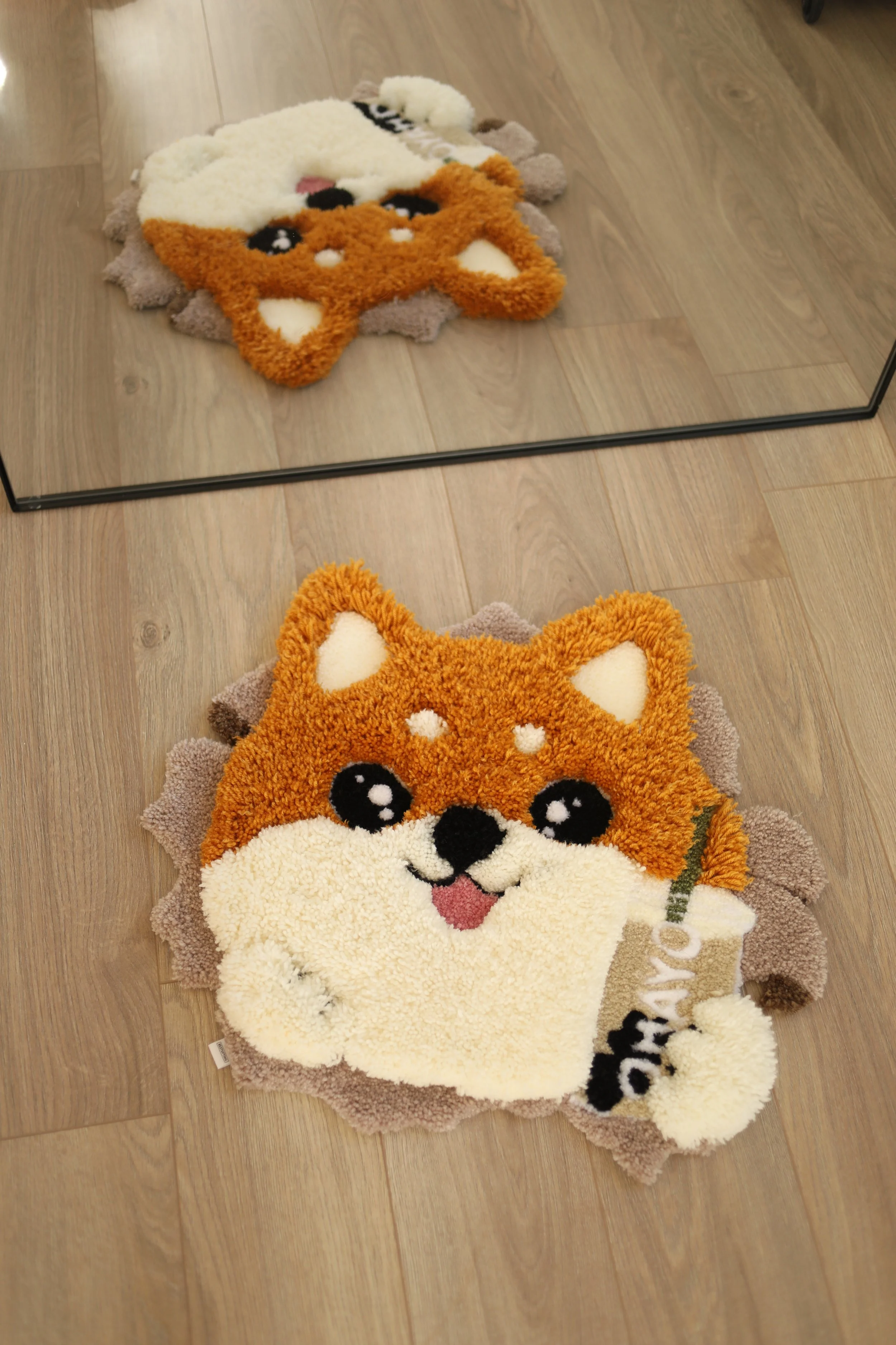 Fluffy rug with a cartoon Shuba Inu holding bubble tea on a wooden floor, visible mirror reflection.