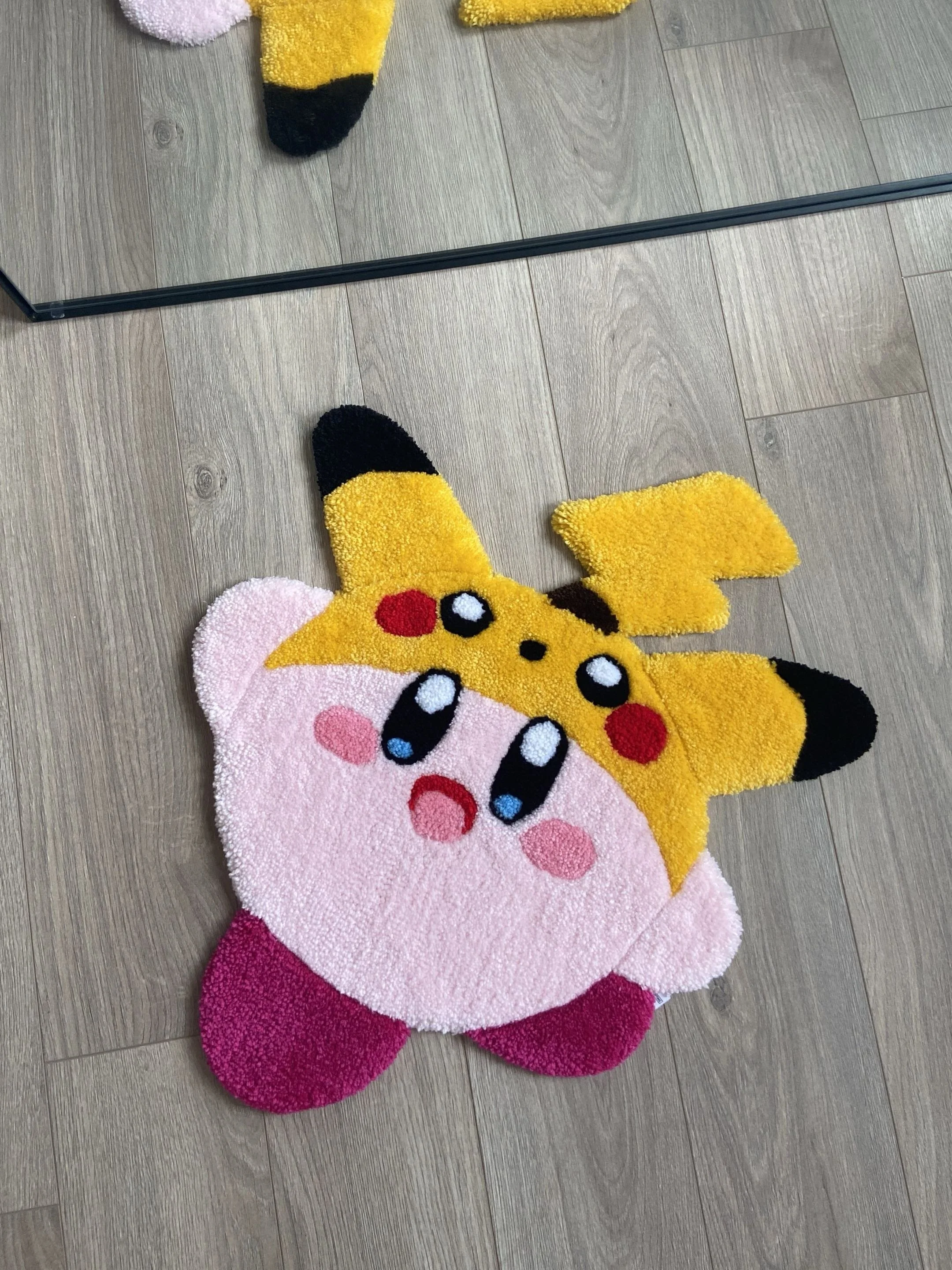Colorful Pikachu and Kirby themed rugs on a wood floor, with a mirror visible in the background.