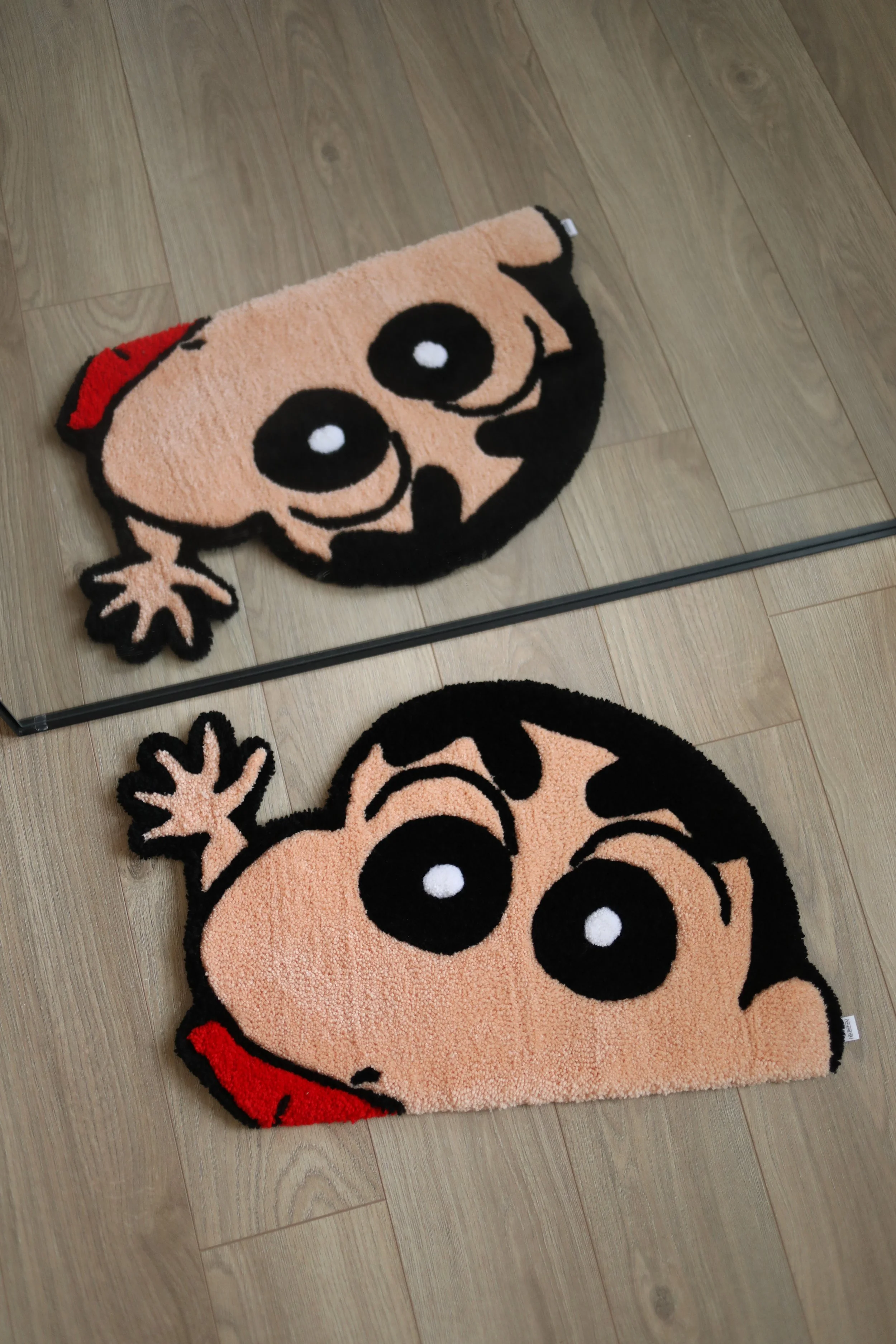 Cartoon character themed doormat featuring a cute, smiling face with large eyes, a red bow, and a red tongue, placed on a wooden floor.