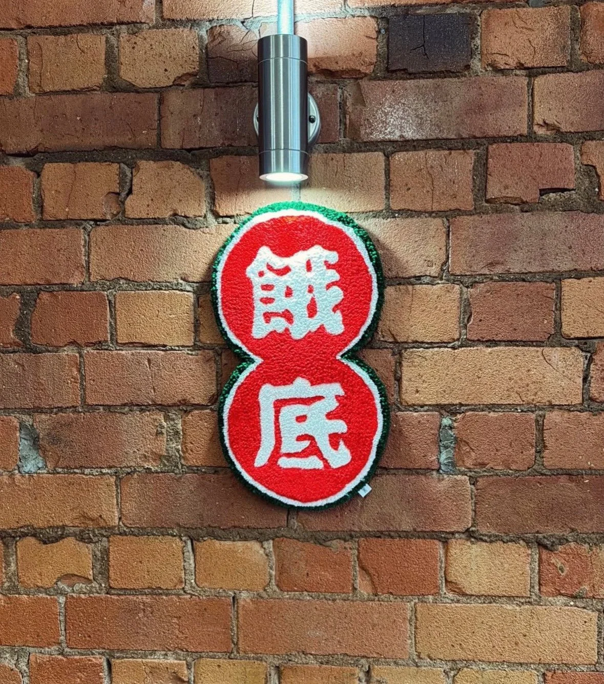 A brick wall with a red circular sign featuring white Chinese characters, illuminated by a small wall-mounted light fixture.