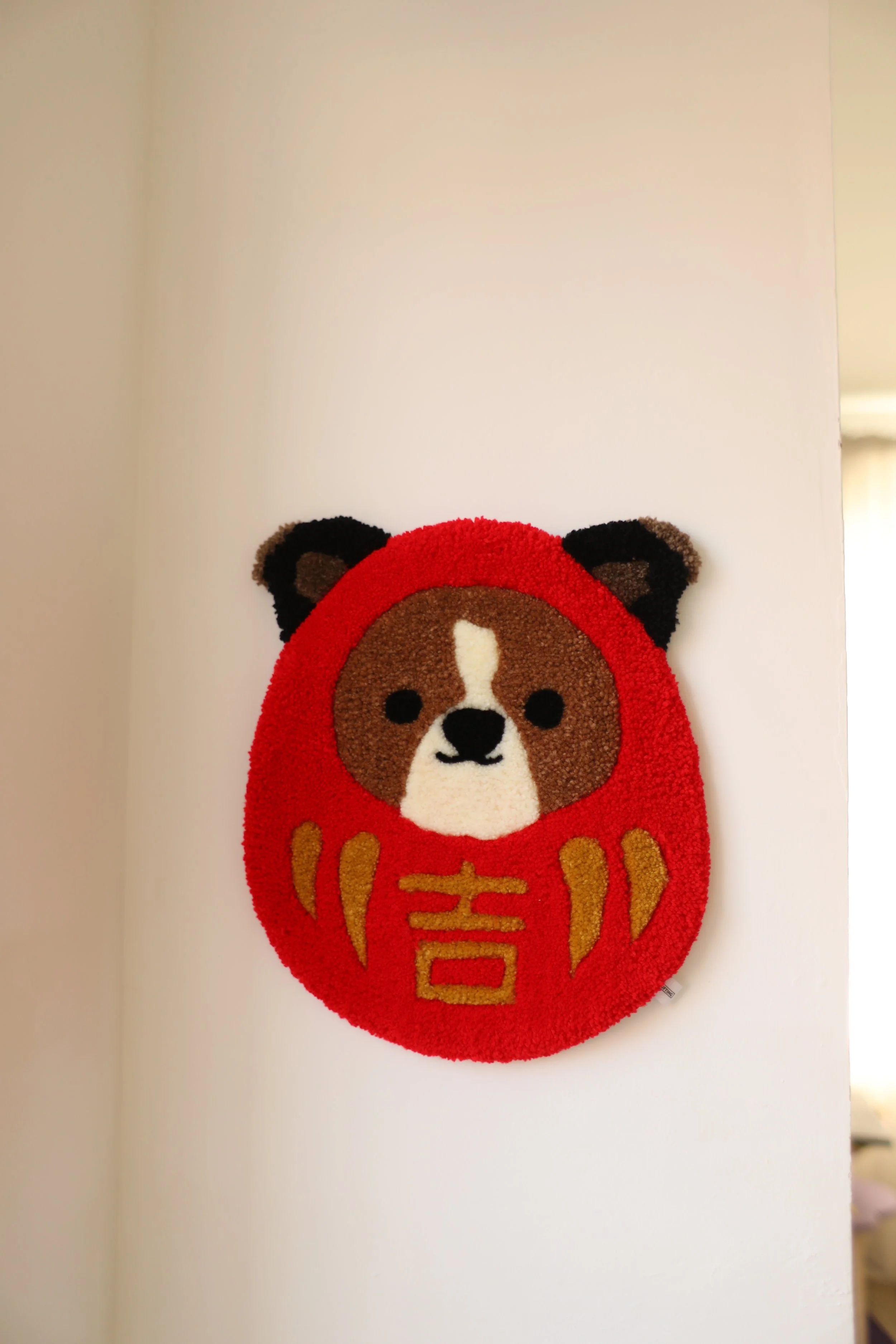 A decorative wall hanging in the shape of a dog as daruma with golden Chinese characters on it.