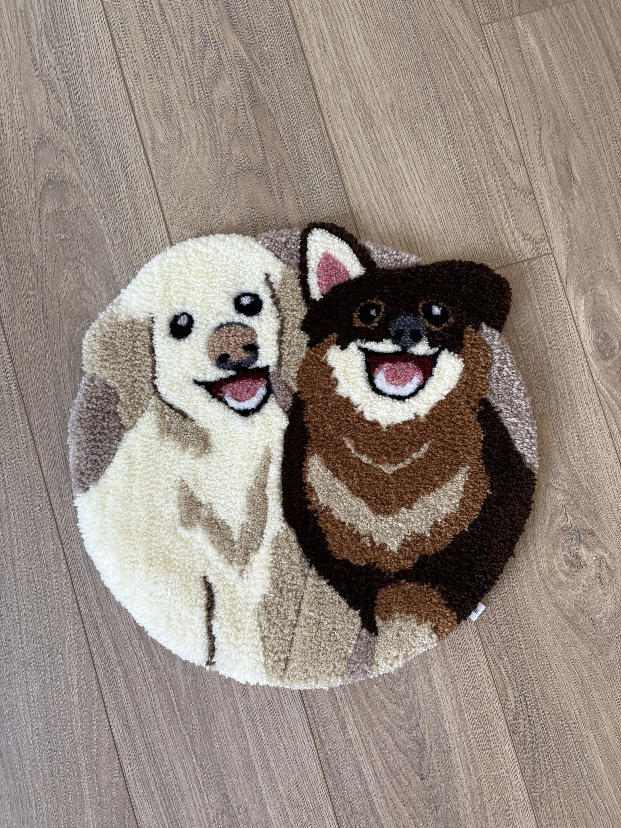 A round plush rug featuring two dogs, one light-colored and one dark-colored, with realistic facial features, on a wooden floor.