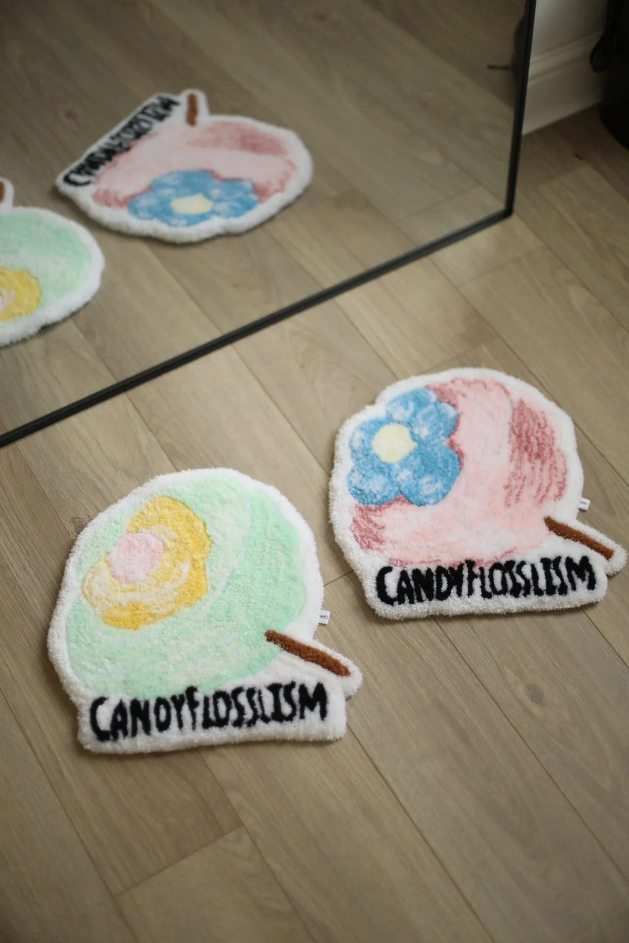 Colourful rugs shaped like candy floss, placed on a wooden floor with a mirror reflecting part of the rugs.