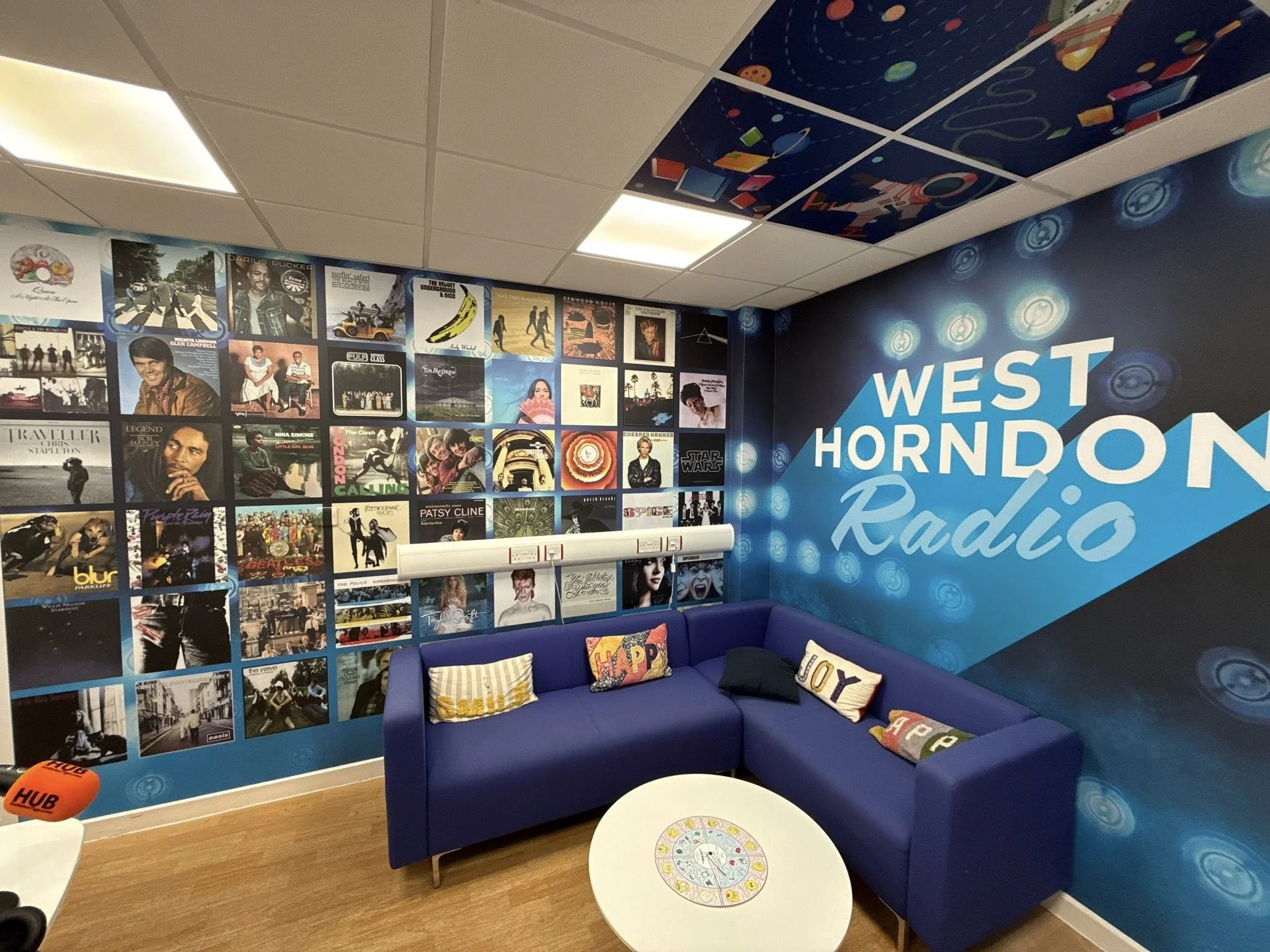 A waiting area with a blue couch, a small round white table, and a decorated wall with posters of music albums and a