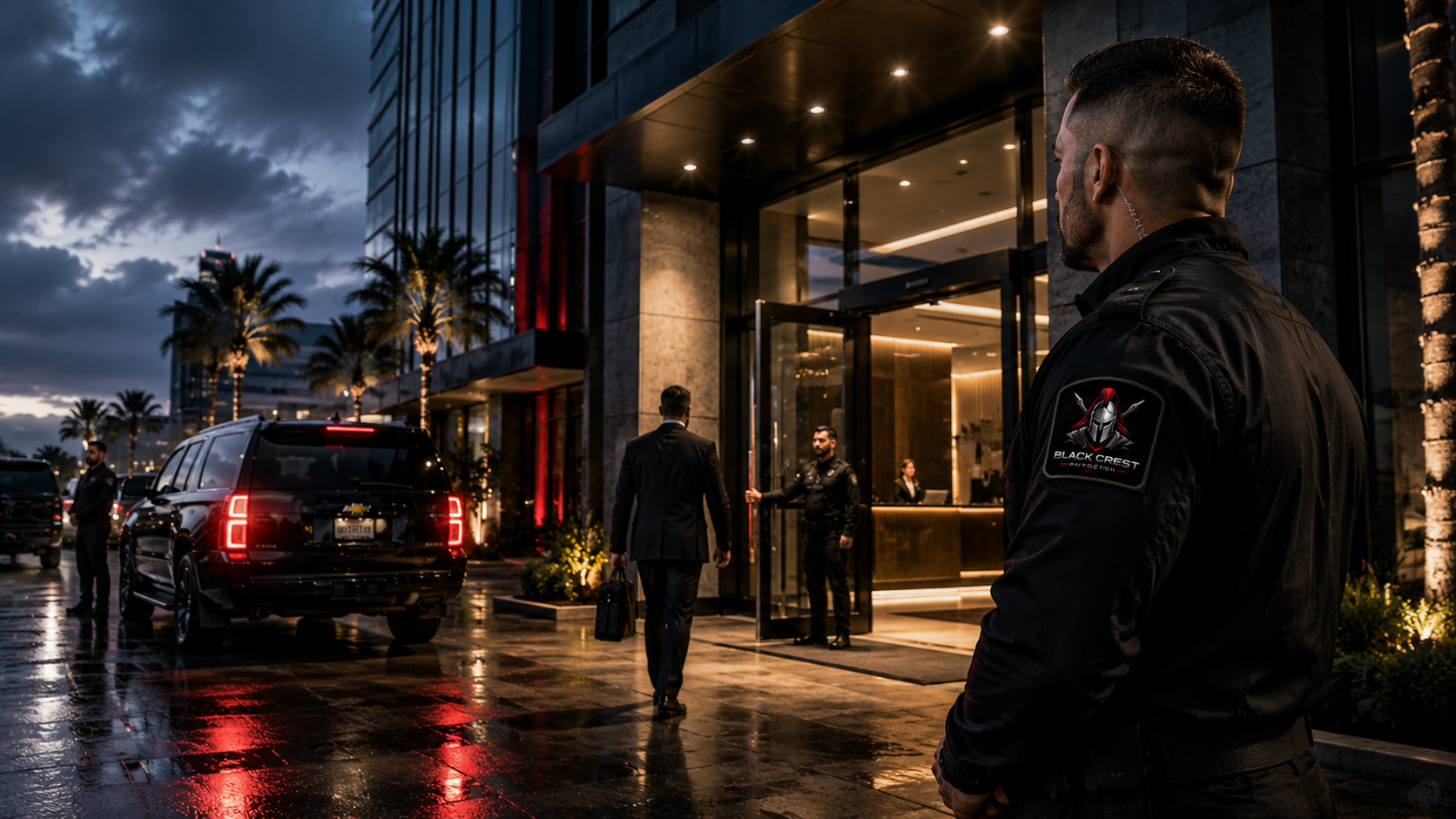 Security personnel in black uniforms with the Black Crest Protection patches monitor the entrance of a modern hotel lobby, with a man in a suit approaching and a black SUV parked outside on a rainy evening.